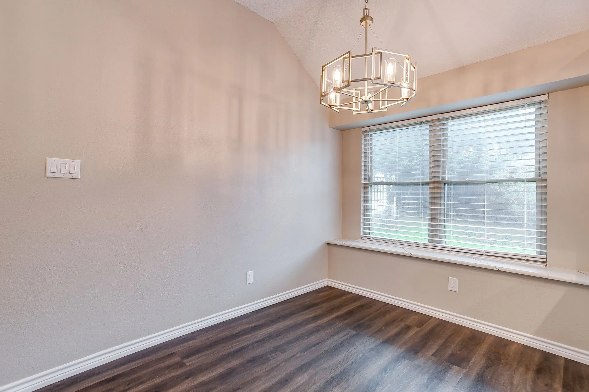 Vaulted ceiling with an architectural chandelier, large window with blinds, and wood-finish flooring