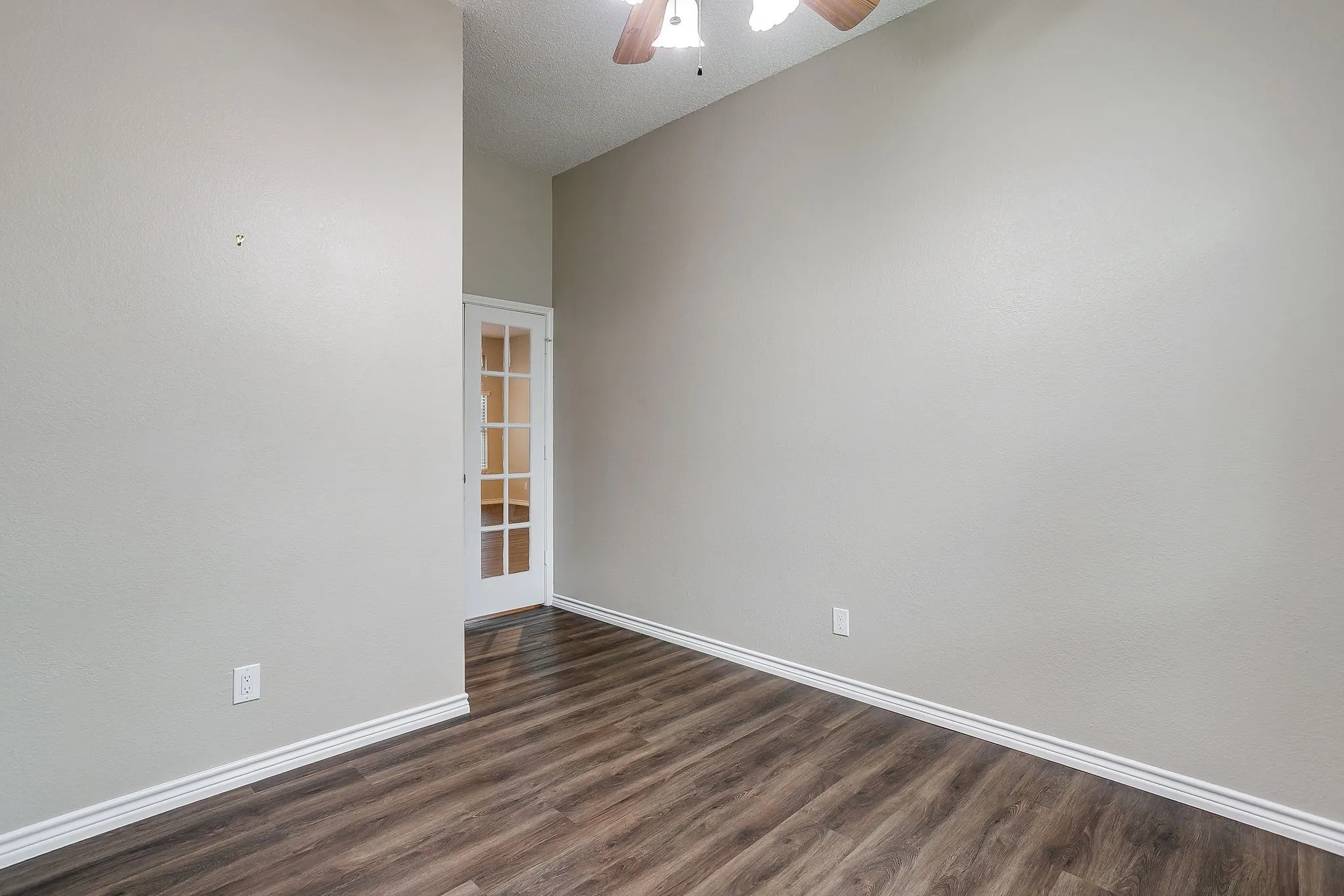 Vaulted ceiling, wood-finish flooring, white baseboards, French doors, and a ceiling fan