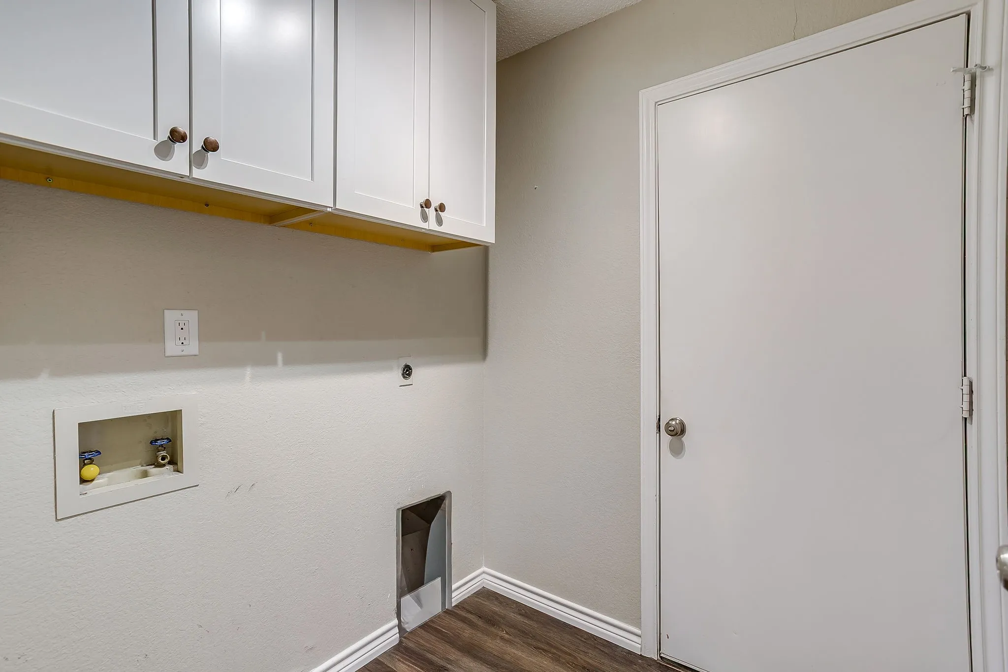 White shaker-style cabinetry with wood-finish knobs, wood-finish flooring, and a utility hookup