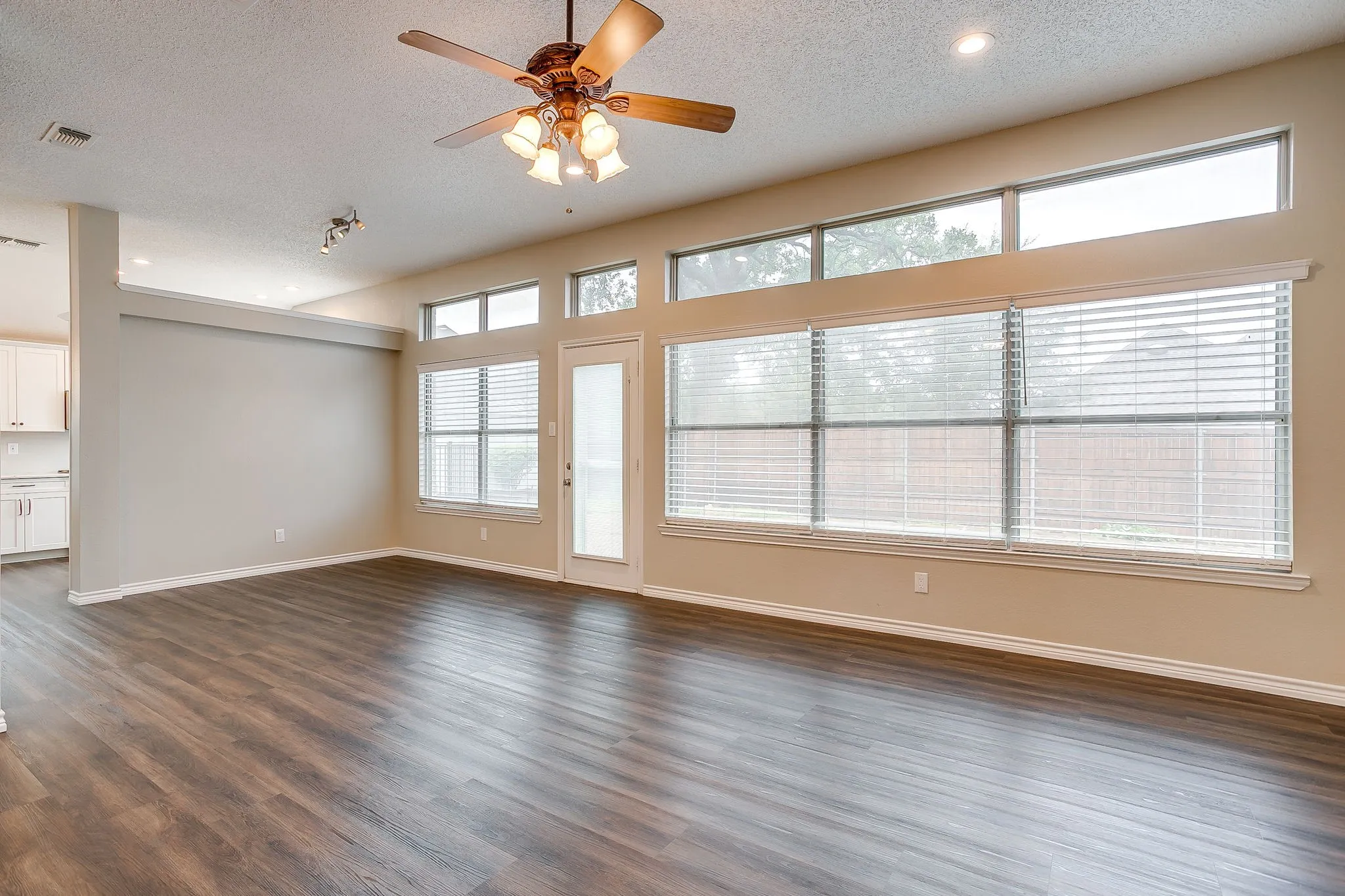 Expansive living area with wood-finish flooring, a ceiling fan, recessed lighting, and a wall of windows topped with transom windows