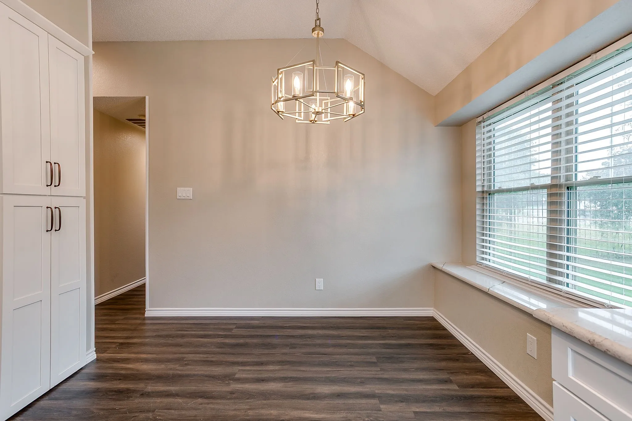 Vaulted ceiling with an architectural chandelier, wood-finish flooring, white built-in cabinetry, and a window with a stone-finish sill