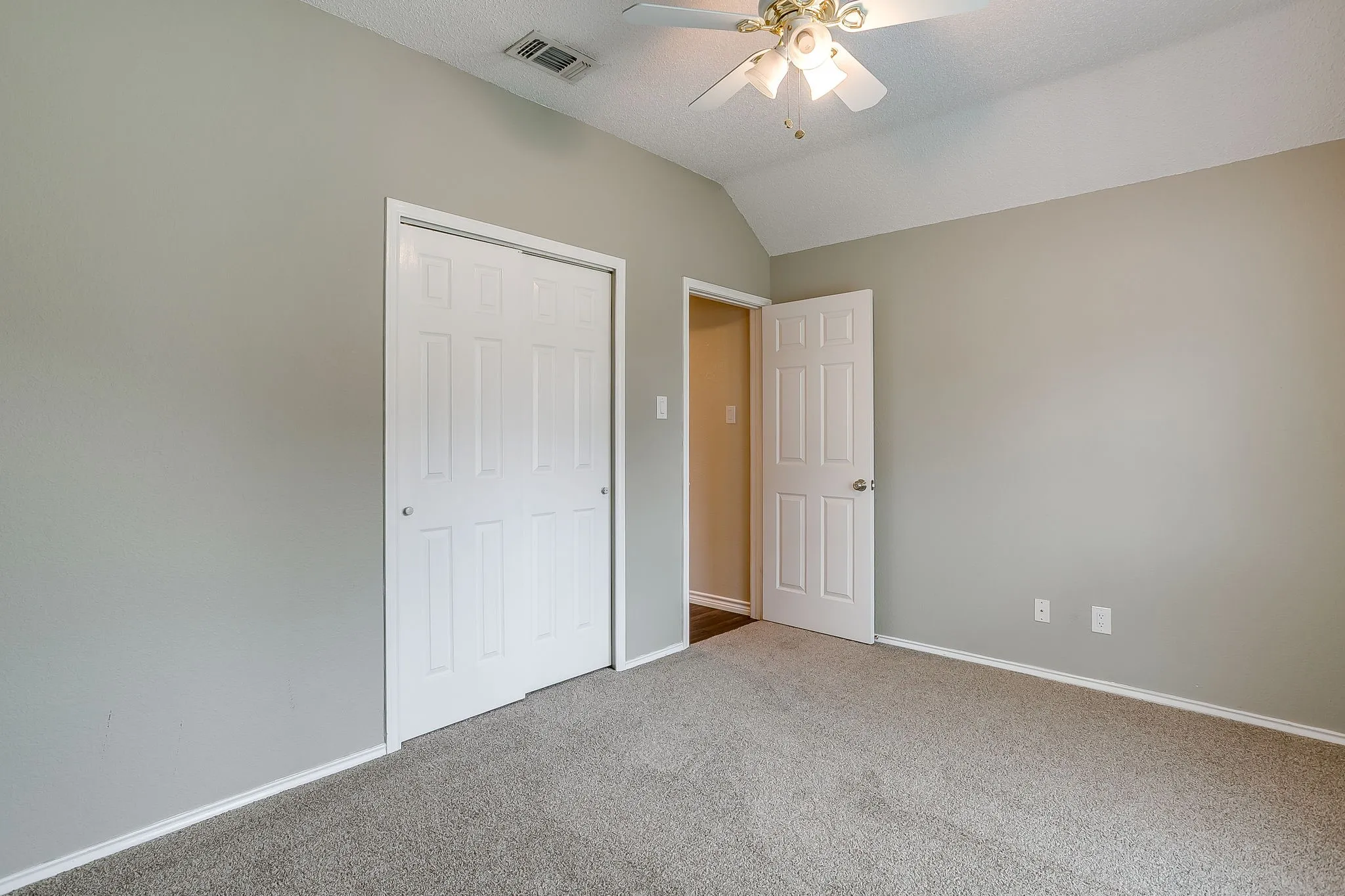 Vaulted ceiling with an attached ceiling fan, neutral wall paint, and gray carpet flooring
