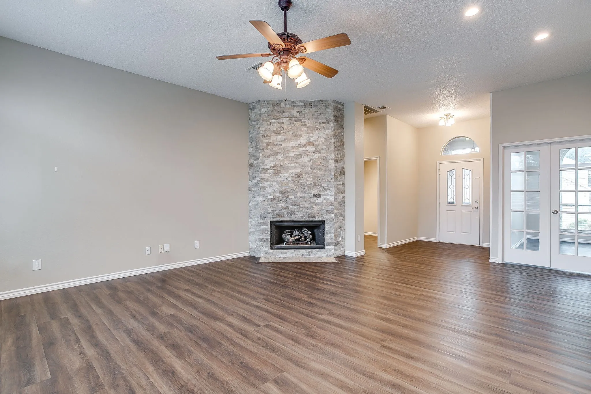 Spacious room featuring wood-finish flooring, a stacked stone fireplace, and a ceiling fan with integrated lighting