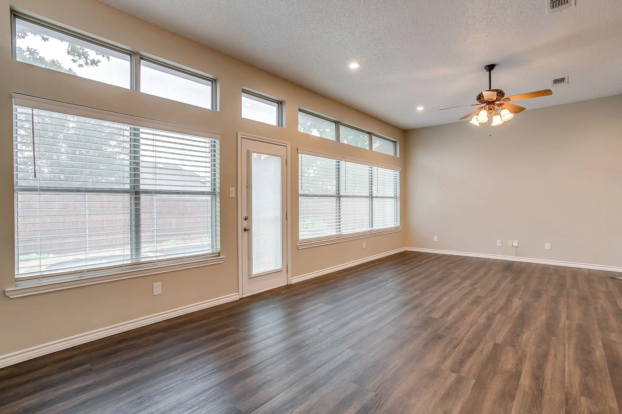 Spacious room featuring wood-finish flooring, abundant natural light from multiple windows, a ceiling fan, and recessed lighting