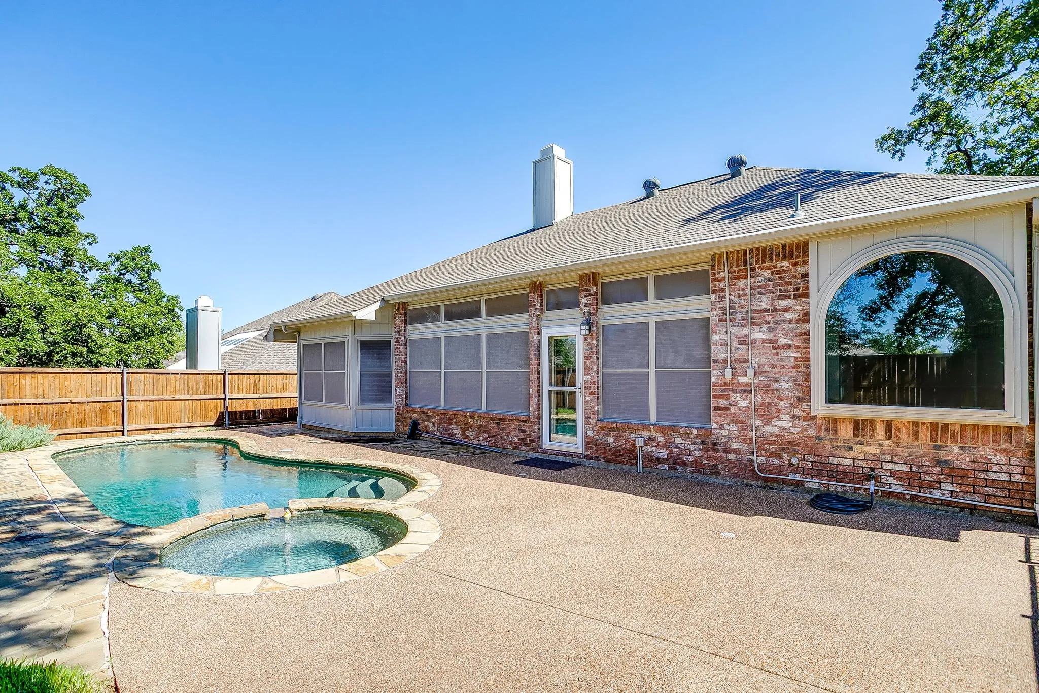 Red brick exterior with an arched window, screened patio, and an outdoor pool with a spa