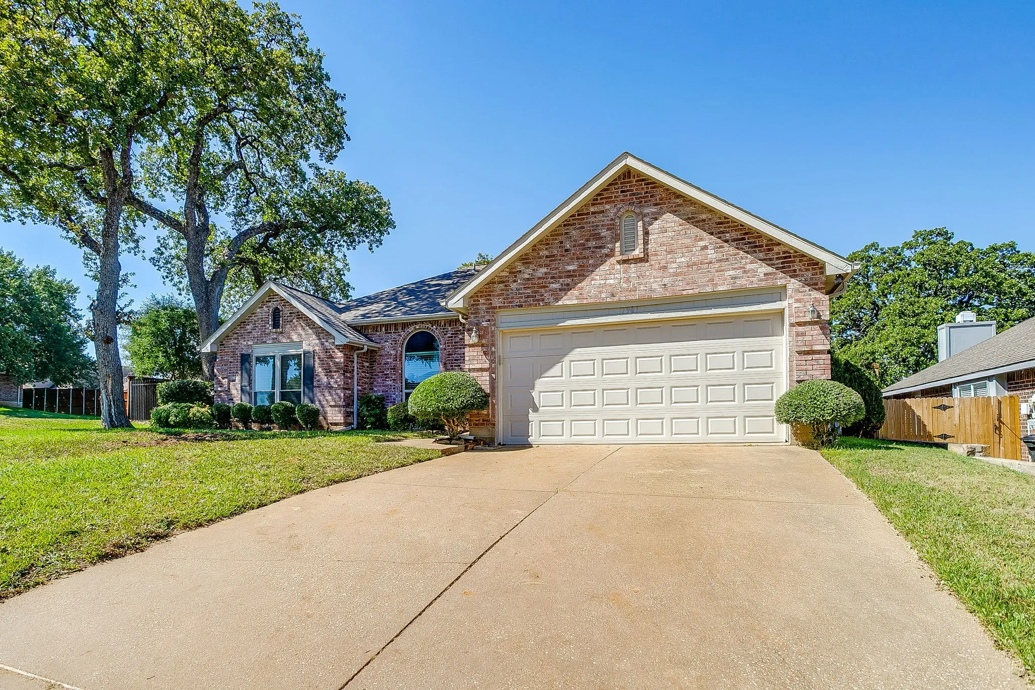 Brick exterior with an attached garage, arched window, and mature trees