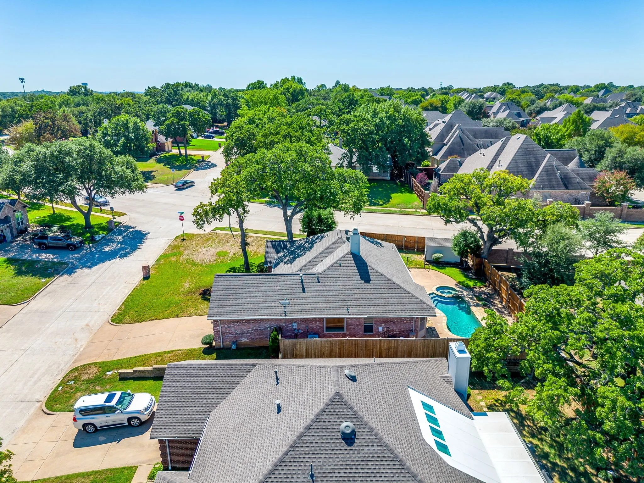 Brick exterior residence featuring an in-ground swimming pool with spa, surrounded by mature trees, and an attached chimney
