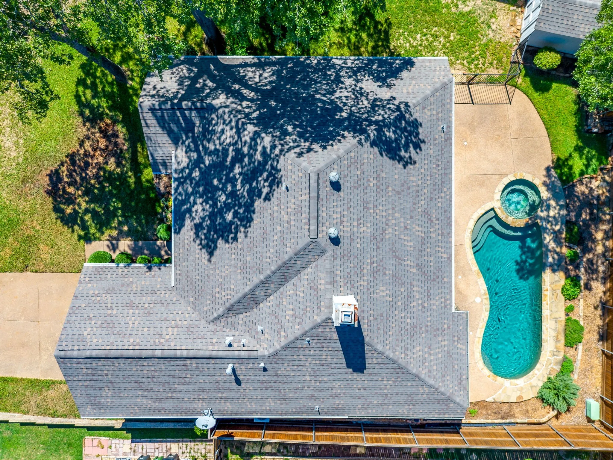 Asphalt shingle roof, paved patio, freeform swimming pool, integrated spa, and manicured landscaping