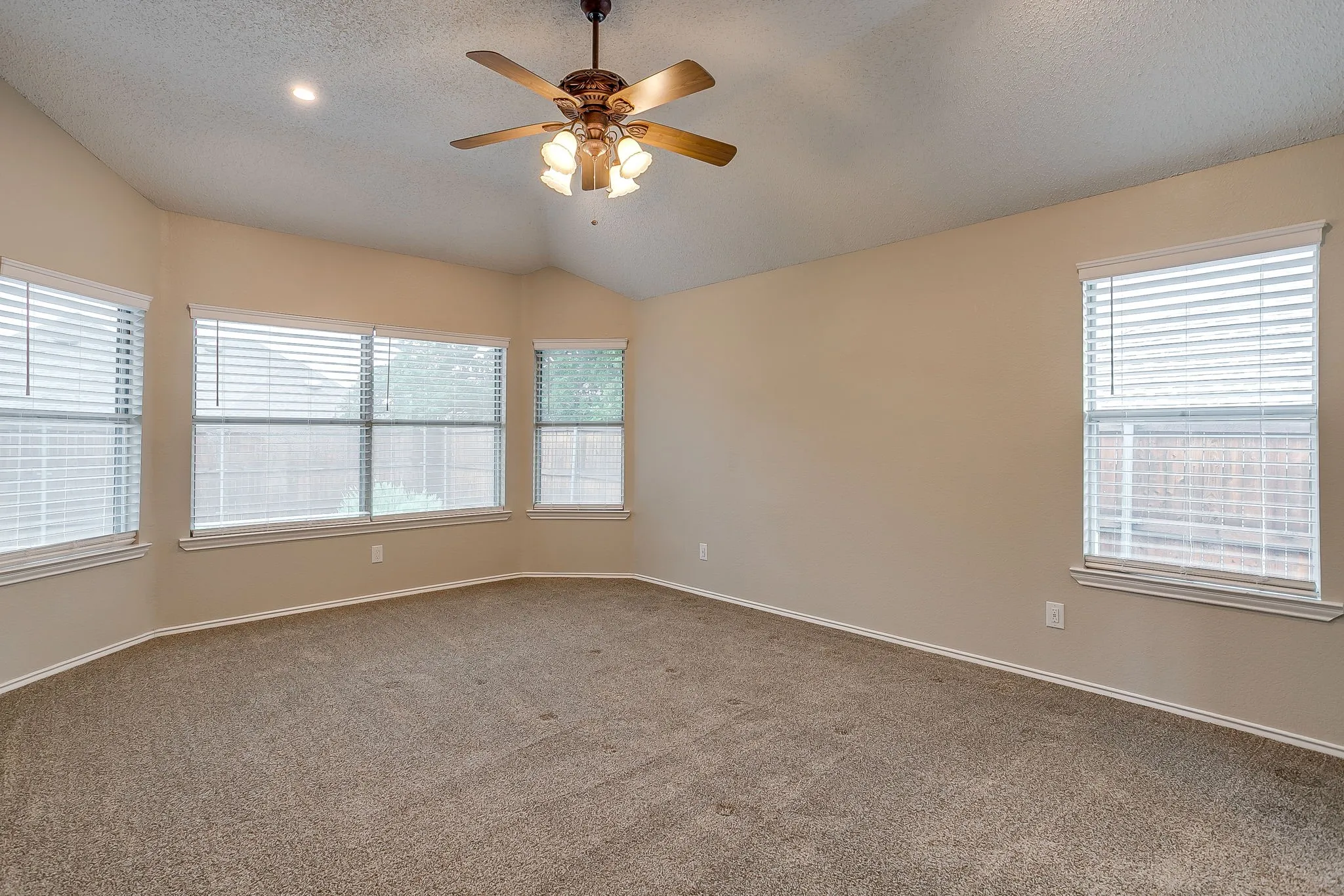 Vaulted ceiling, ceiling fan with light kit, recessed lighting, multiple windows with blinds, and neutral carpeting