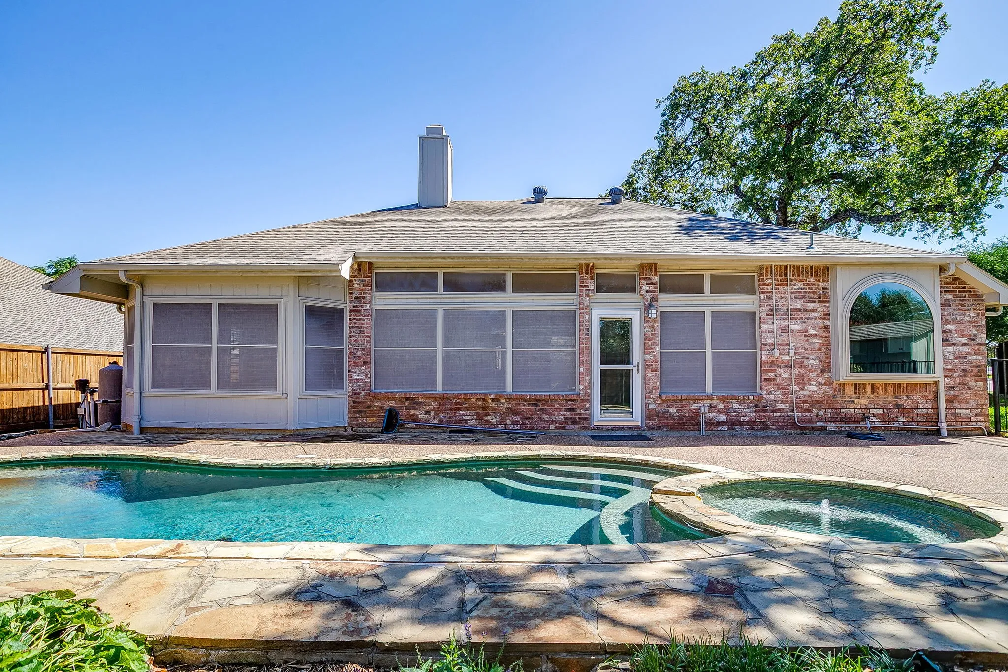 Brick exterior with screened-in porch, large arched window, and a built-in pool with an integrated spa