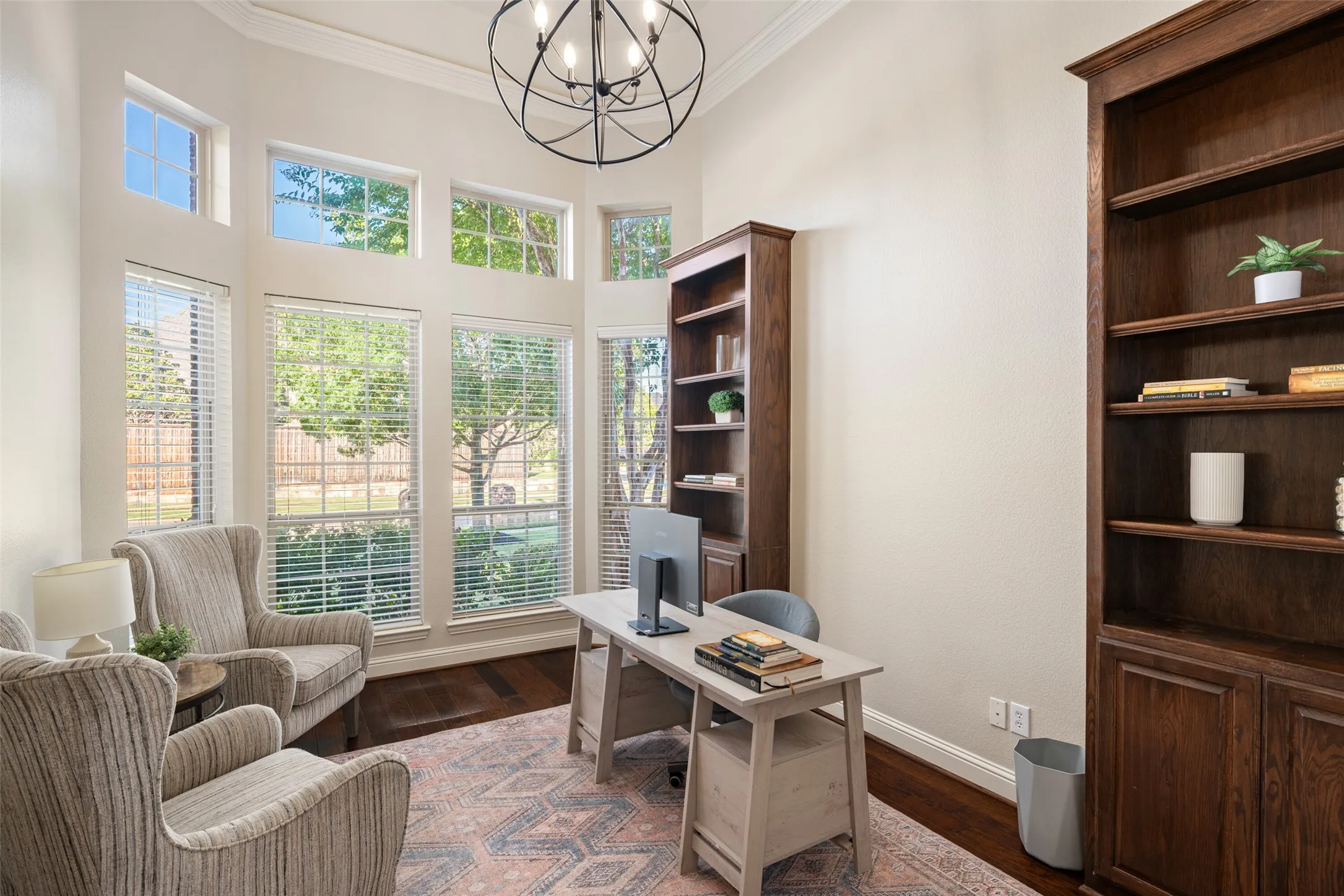 Two-story space featuring a floor-to-ceiling window arrangement, rich wood-finish flooring, a contemporary chandelier, and built-in wood shelving