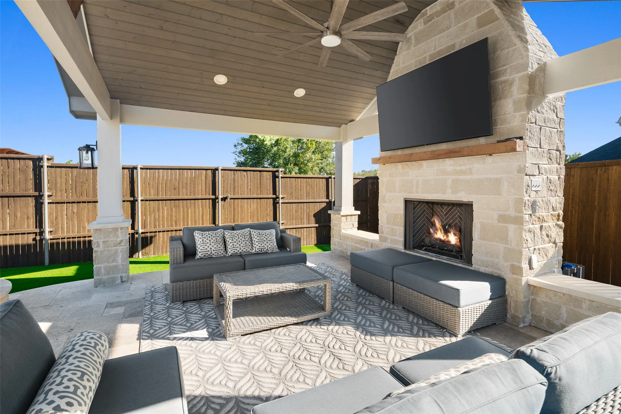 Covered outdoor patio featuring a stone fireplace with wood mantel, a ceiling fan, and recessed lighting