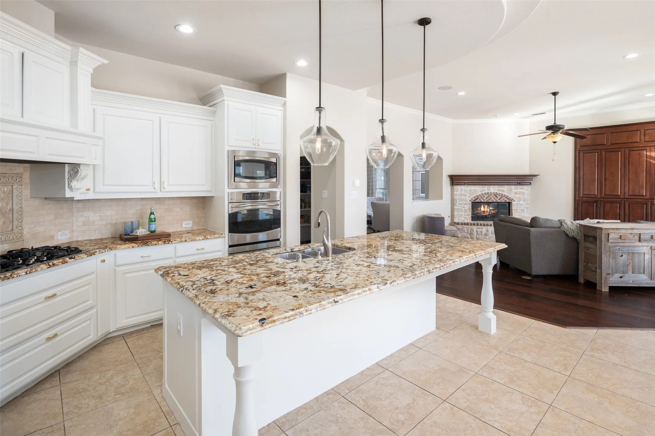 Kitchen with granite countertops, stainless steel built-in appliances, a gas cooktop, white cabinetry, and a large central island with pendant lighting