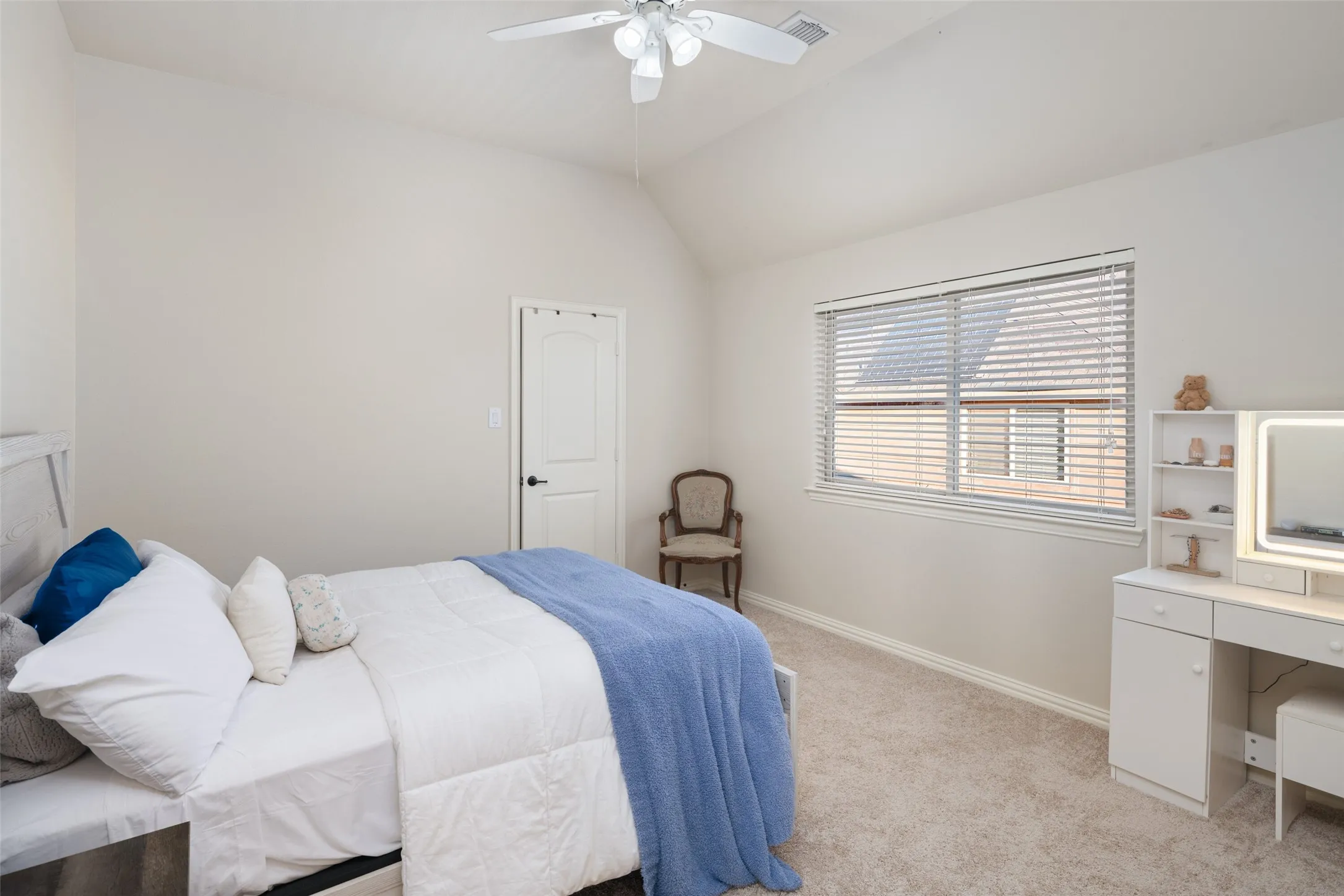 Vaulted ceiling, ceiling fan, white paneled door, window with horizontal blinds, and neutral carpet flooring