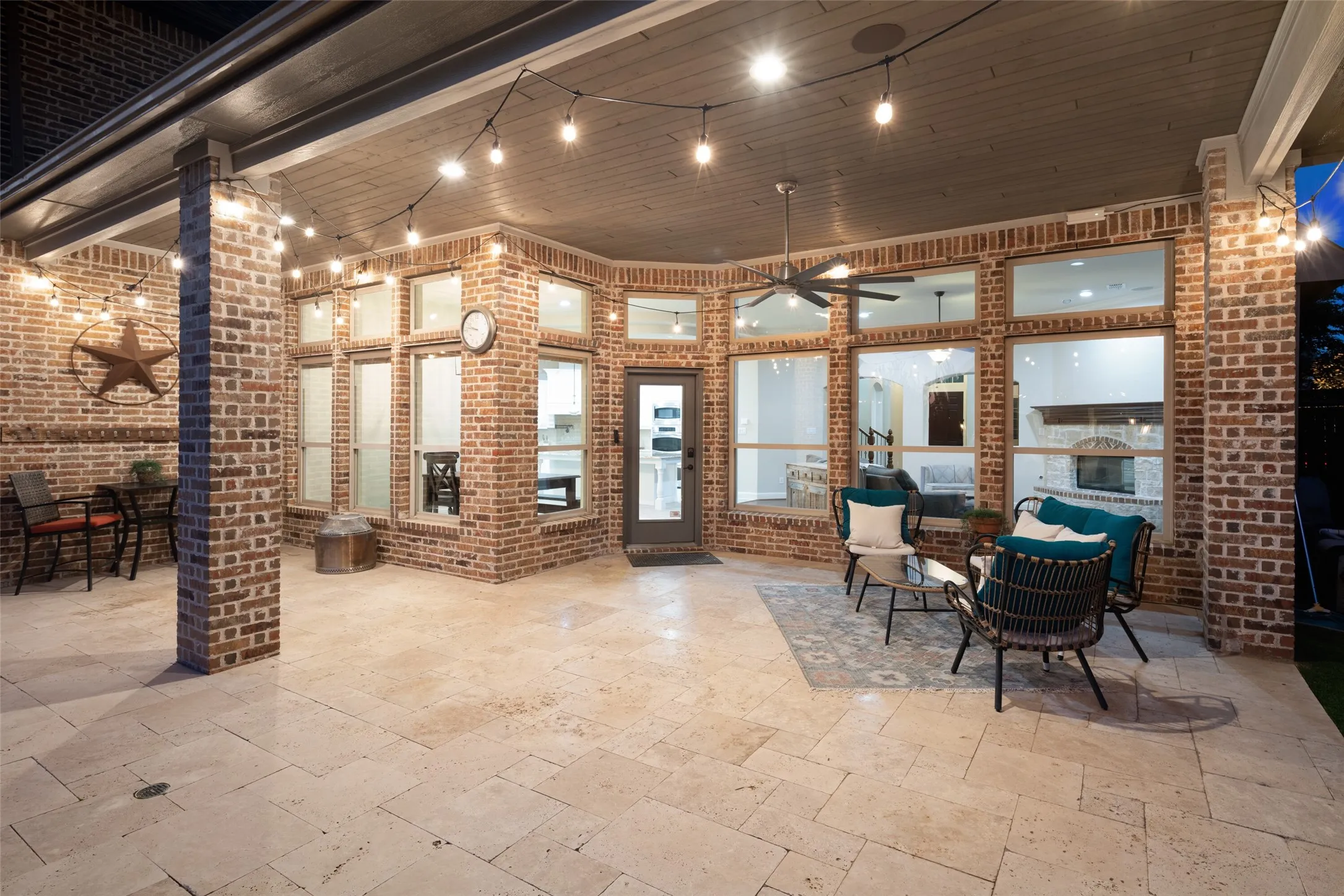 Expansive covered patio featuring brick columns and walls, string lighting, a ceiling fan, and large tile flooring