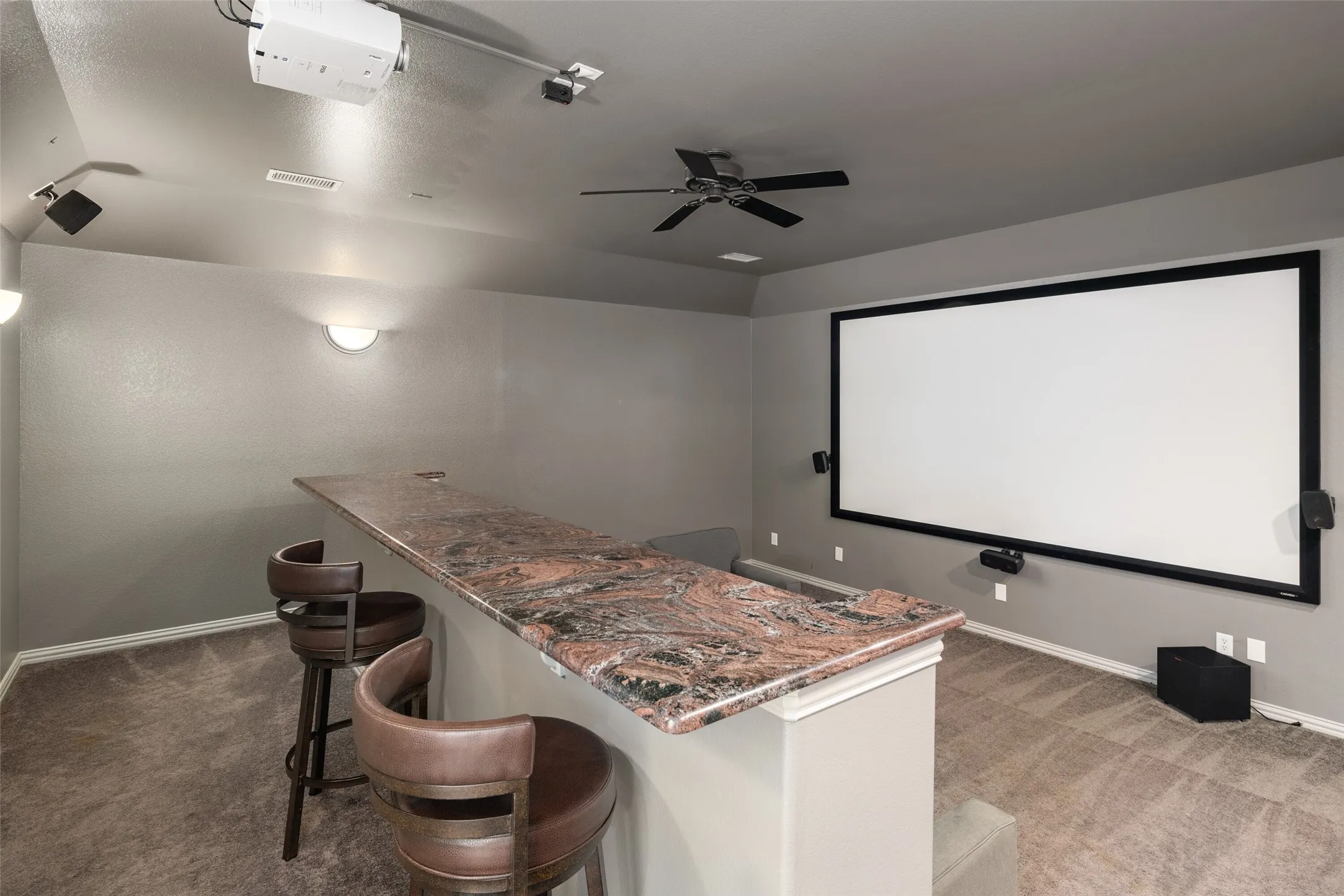Integrated projection screen, ceiling-mounted projector, built-in bar with stone countertop, ceiling fan, and recessed lighting