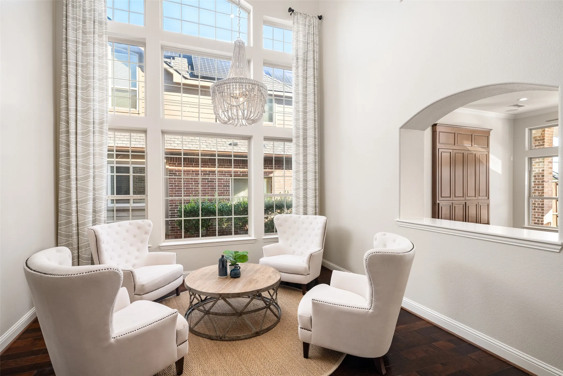 Two-story window wall, wood-finish flooring, vaulted ceiling, arched pass-through, and a decorative chandelier