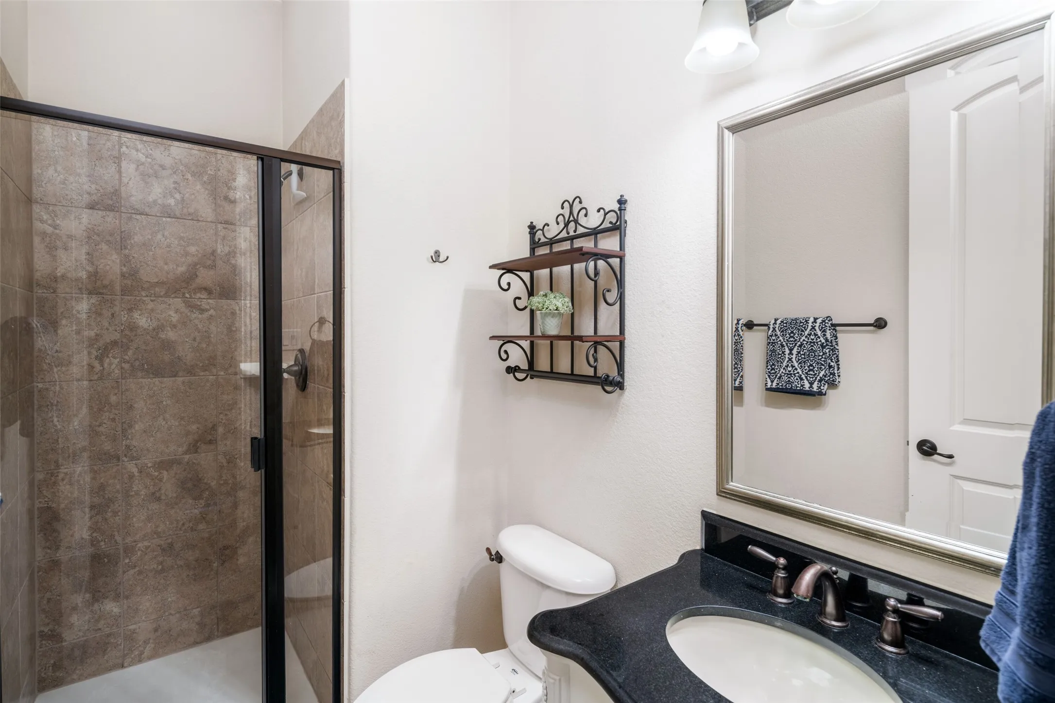 Enclosed shower with tiled walls, dark-framed glass door, and integrated shelving