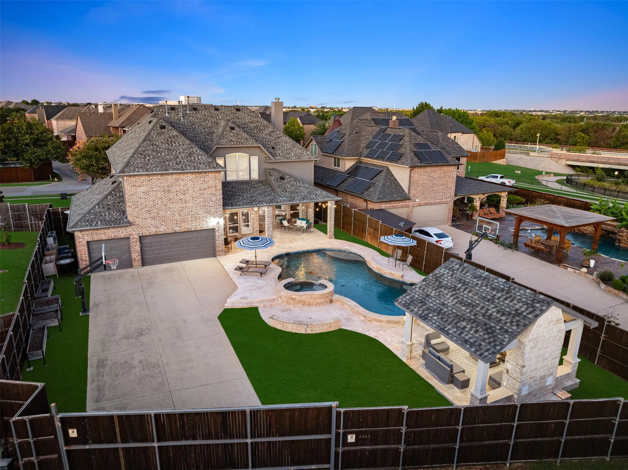 Expansive backyard featuring a custom pool with integrated spa, an outdoor kitchen with a covered patio, a separate stone-clad cabana, and a large concrete patio
