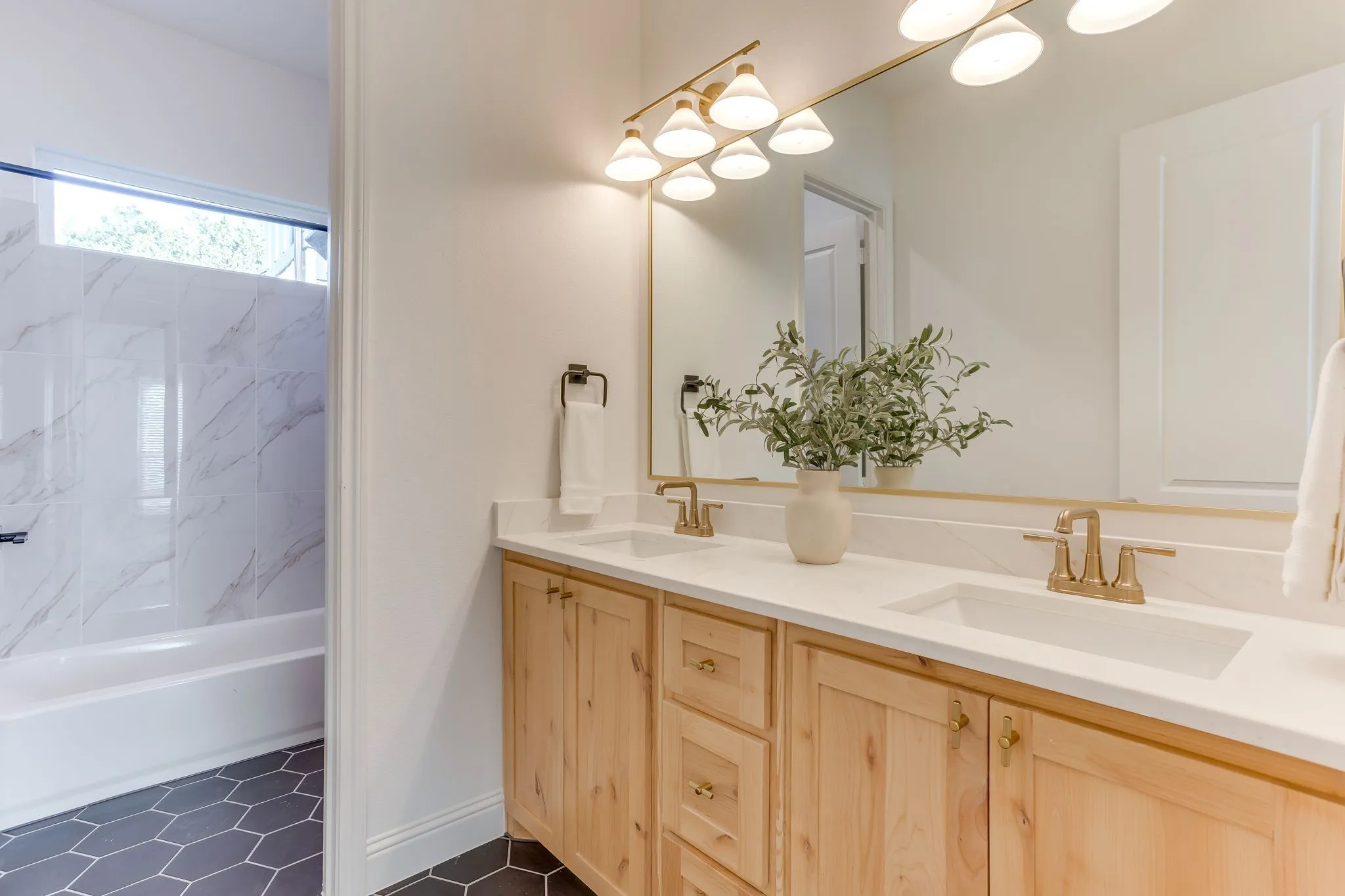 Dual vanity, light wood cabinetry, and gold-tone fixtures
