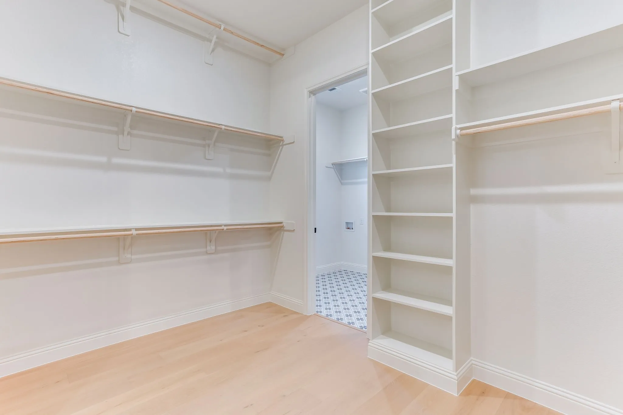 Spacious walk-in closet featuring light wood-finish flooring, multiple hanging rods, and integrated shelving units