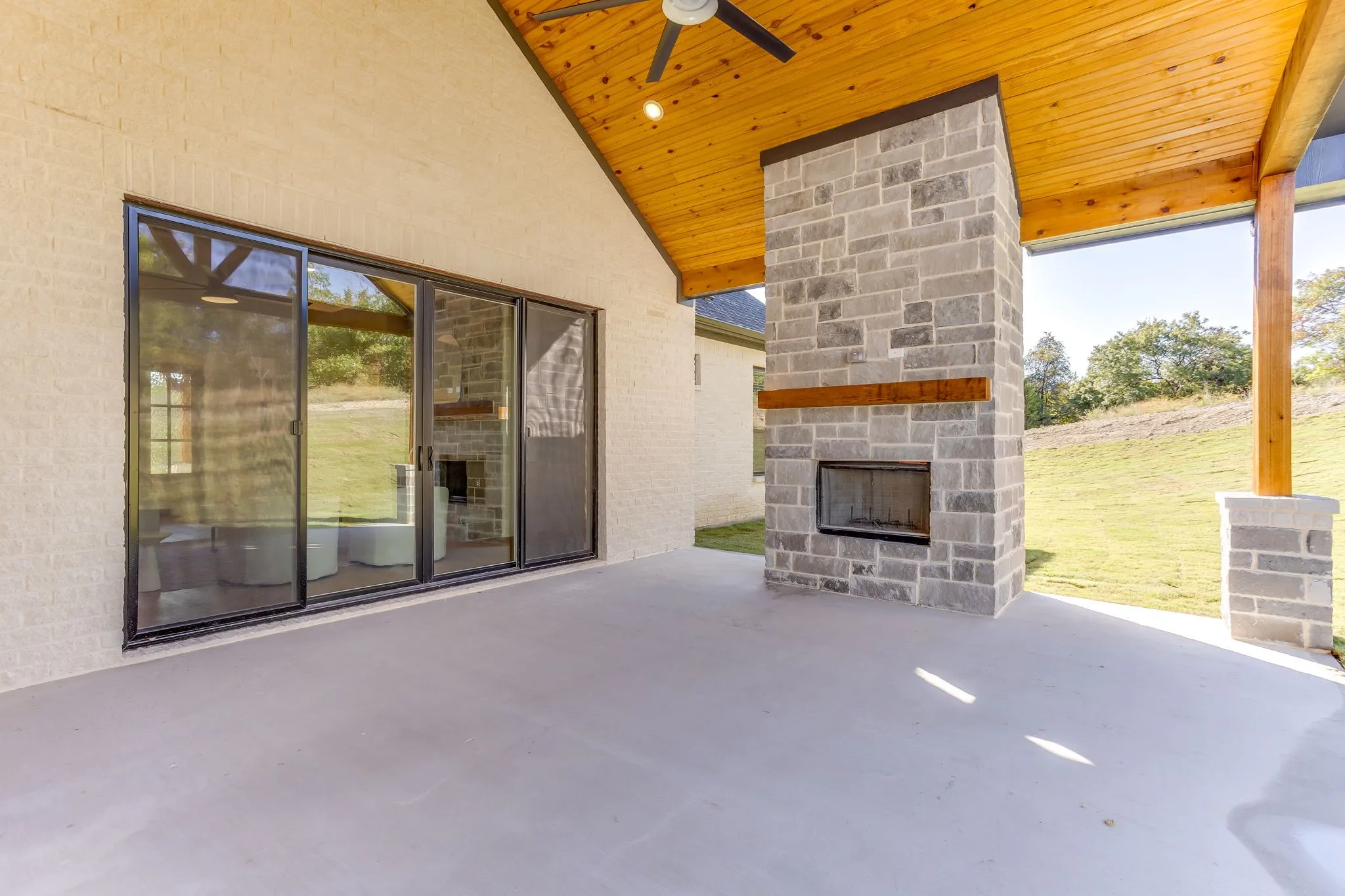 Covered patio featuring a stone fireplace with wood mantel, a high vaulted wood-paneled ceiling, and sliding glass doors