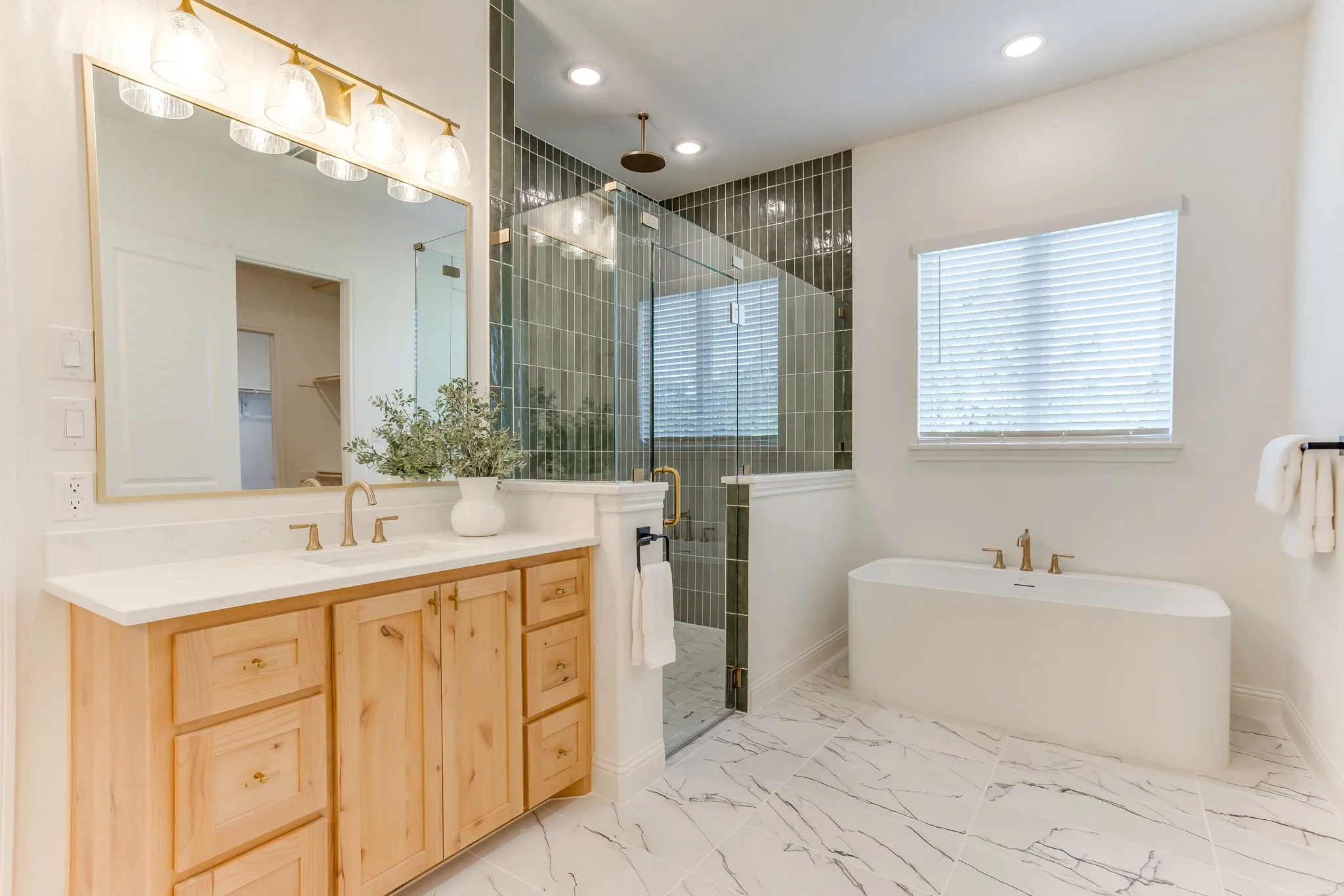 Light wood-finish vanity with a Quartz countertop and gold-finish fixtures and large walk in shower with rainhead