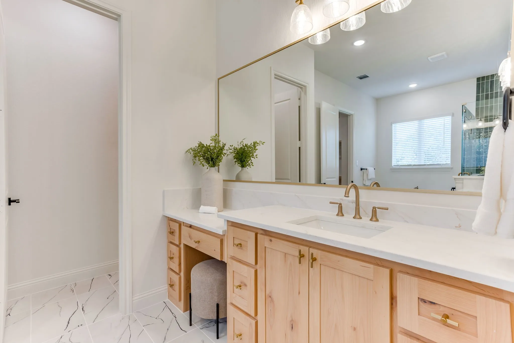 Spa-inspired primary bathroom featuring a wood-finish vanity with ample storage, white Quartz countertop, and brushed gold fixtures