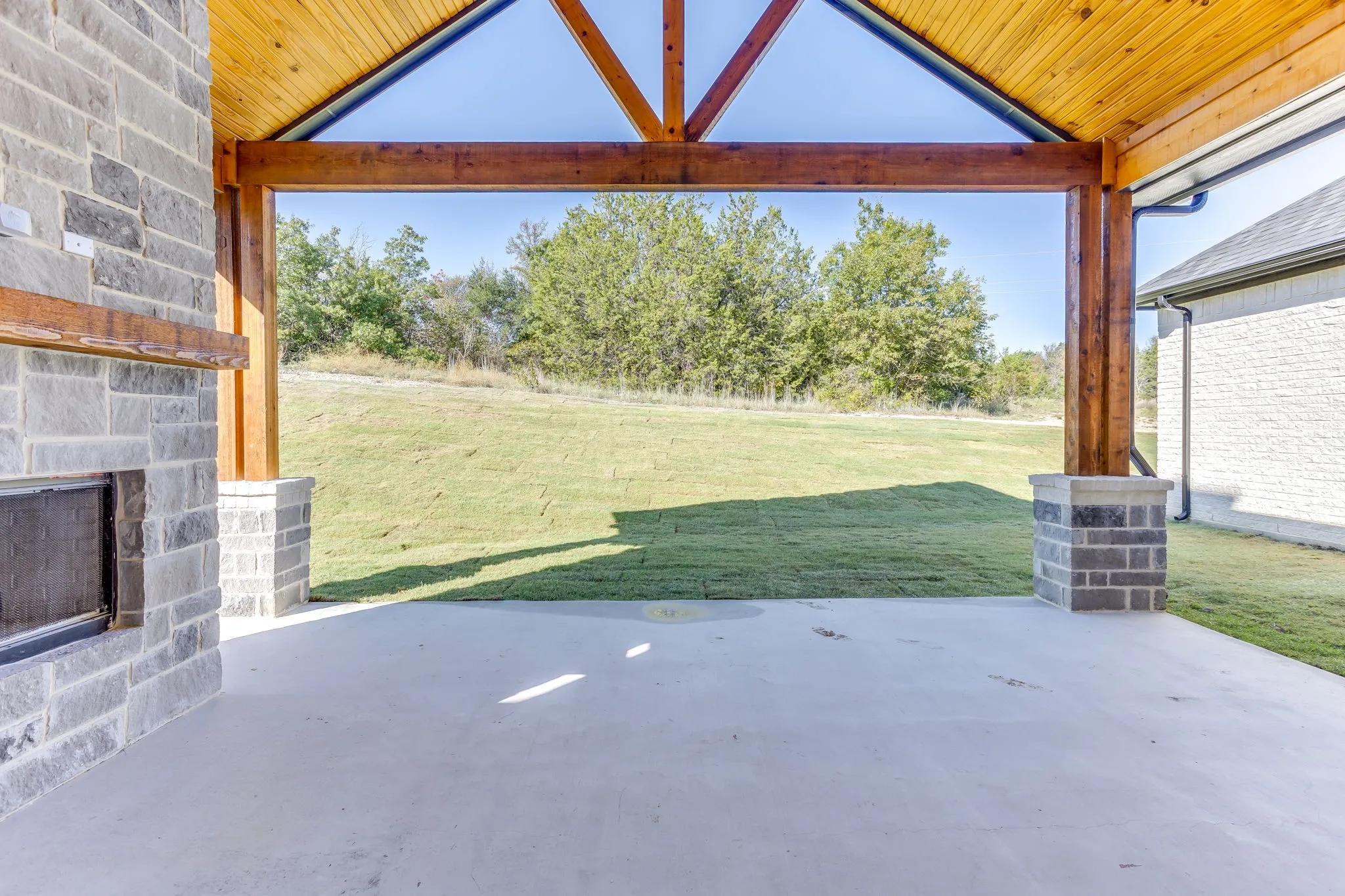 Covered patio with a stone fireplace and wood beam ceiling
