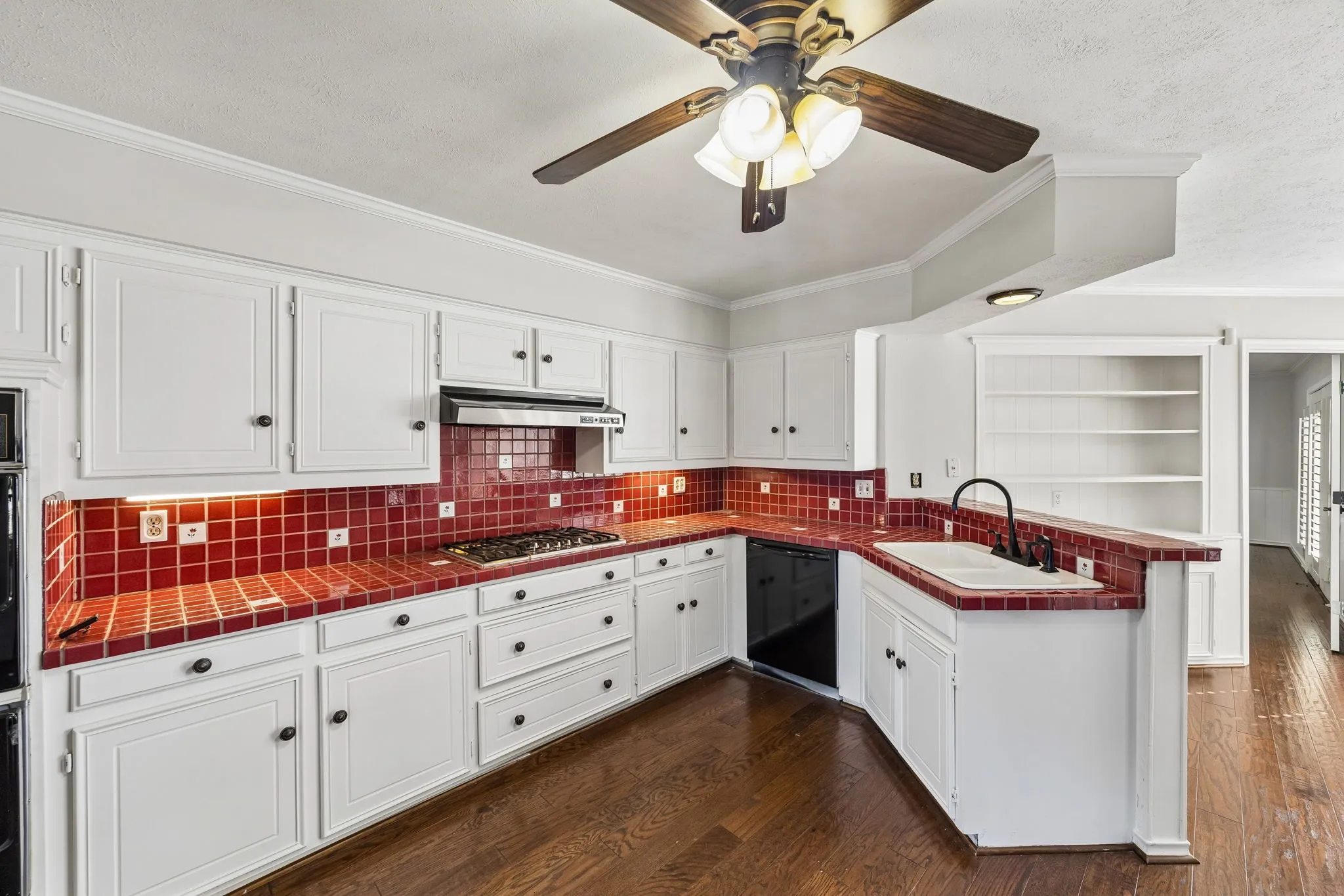 Spacious kitchen featuring white cabinetry with black hardware, red tile backsplash, hardwood flooring, and ample counter space across an L-shaped layout