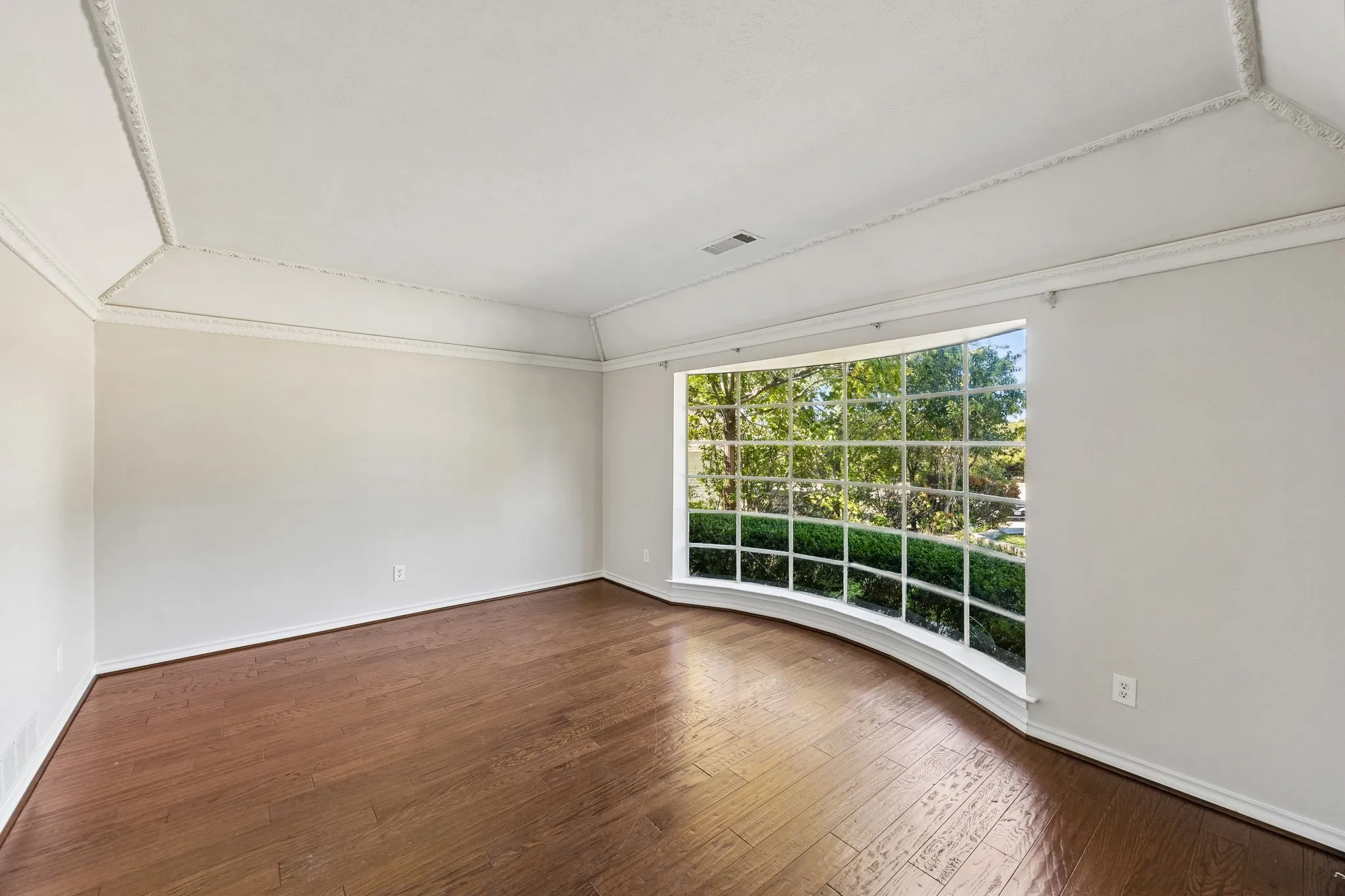 Second living room showcasing hardwood flooring, freshly painted walls, and an expansive multi-pane window wall with natural light and outdoor scenery. This room is also a perfect in-home office.