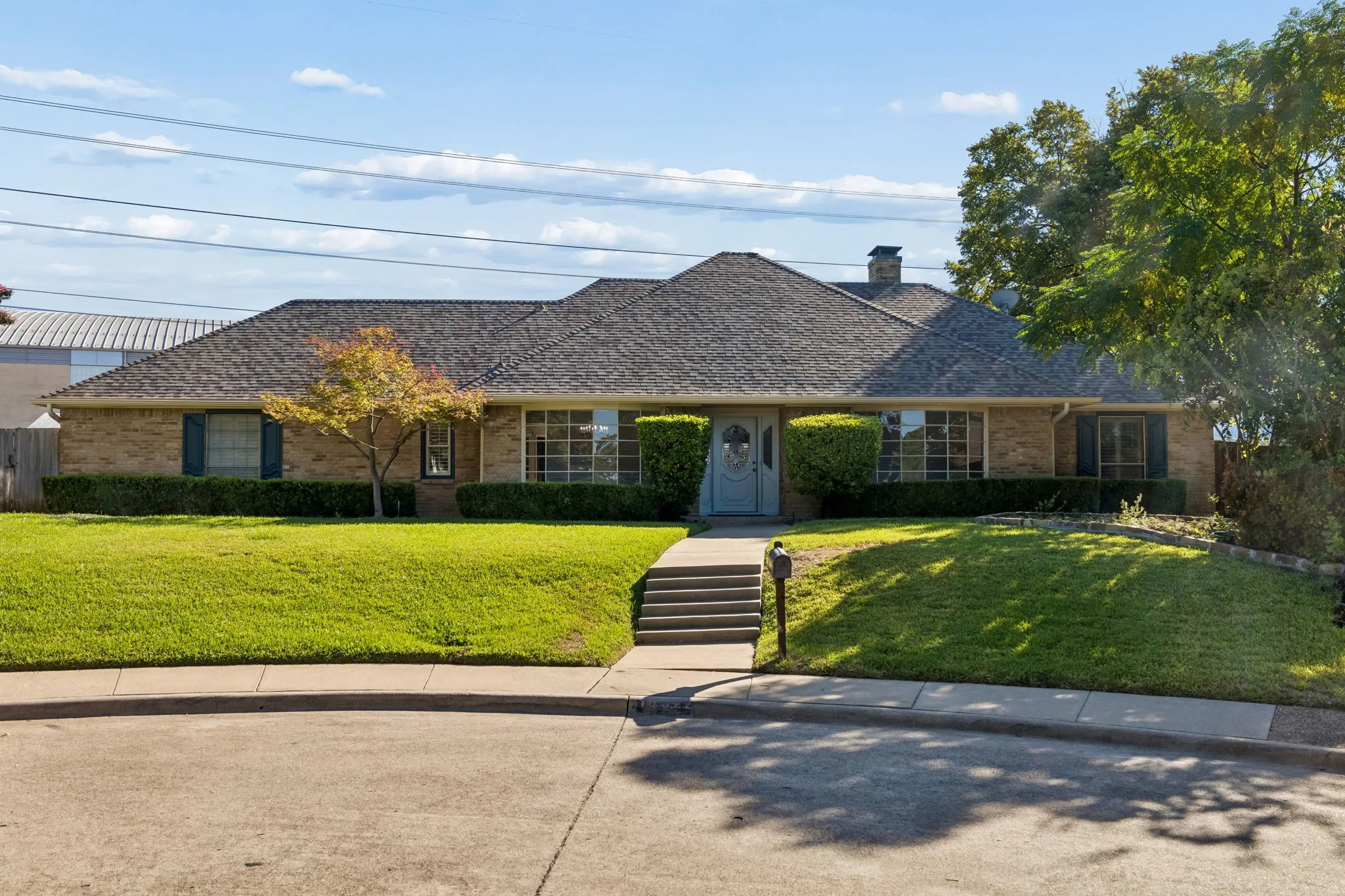 Charming brick ranch featuring a sweeping front lawn with mature landscaping, a welcoming covered entry with stepped walkway