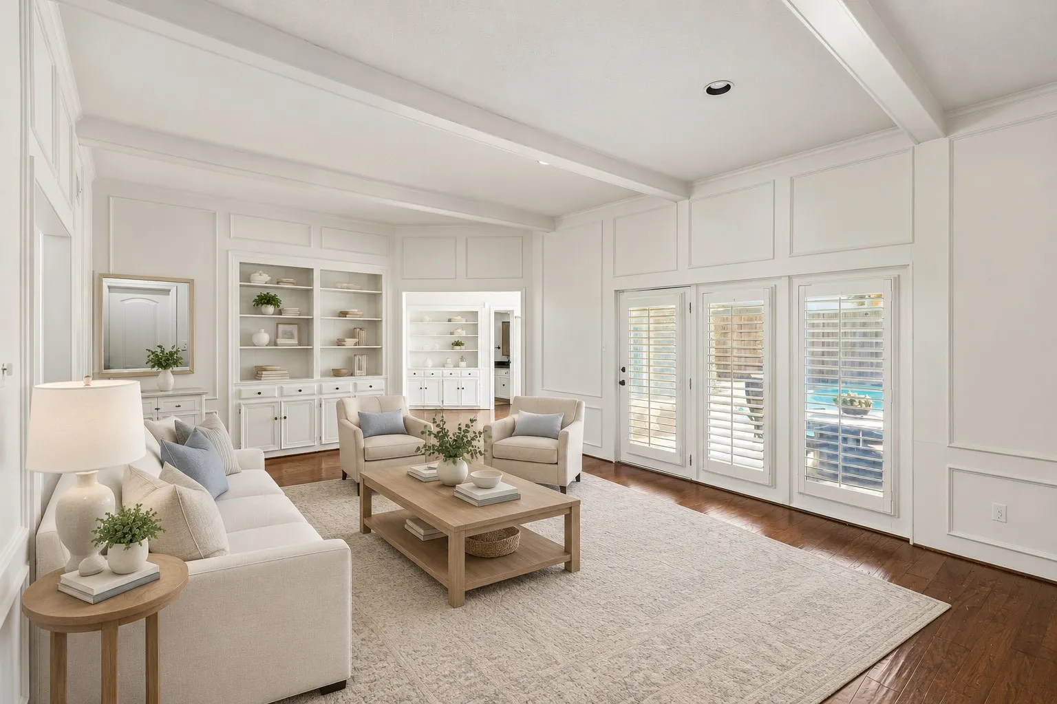 Bright, open-concept main living room featuring coffered ceilings, hardwoods, and abundant natural light from multiple French doors with plantation shutters. This photo is virtually staged.