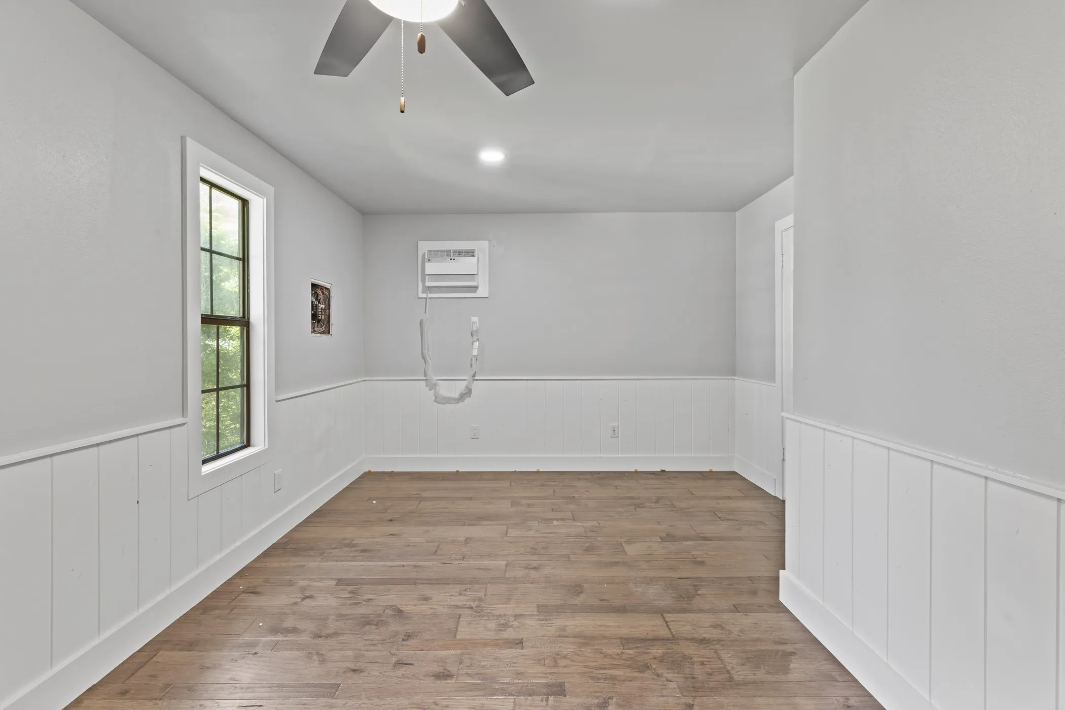 Wood-finish flooring with white wainscoting and a single window