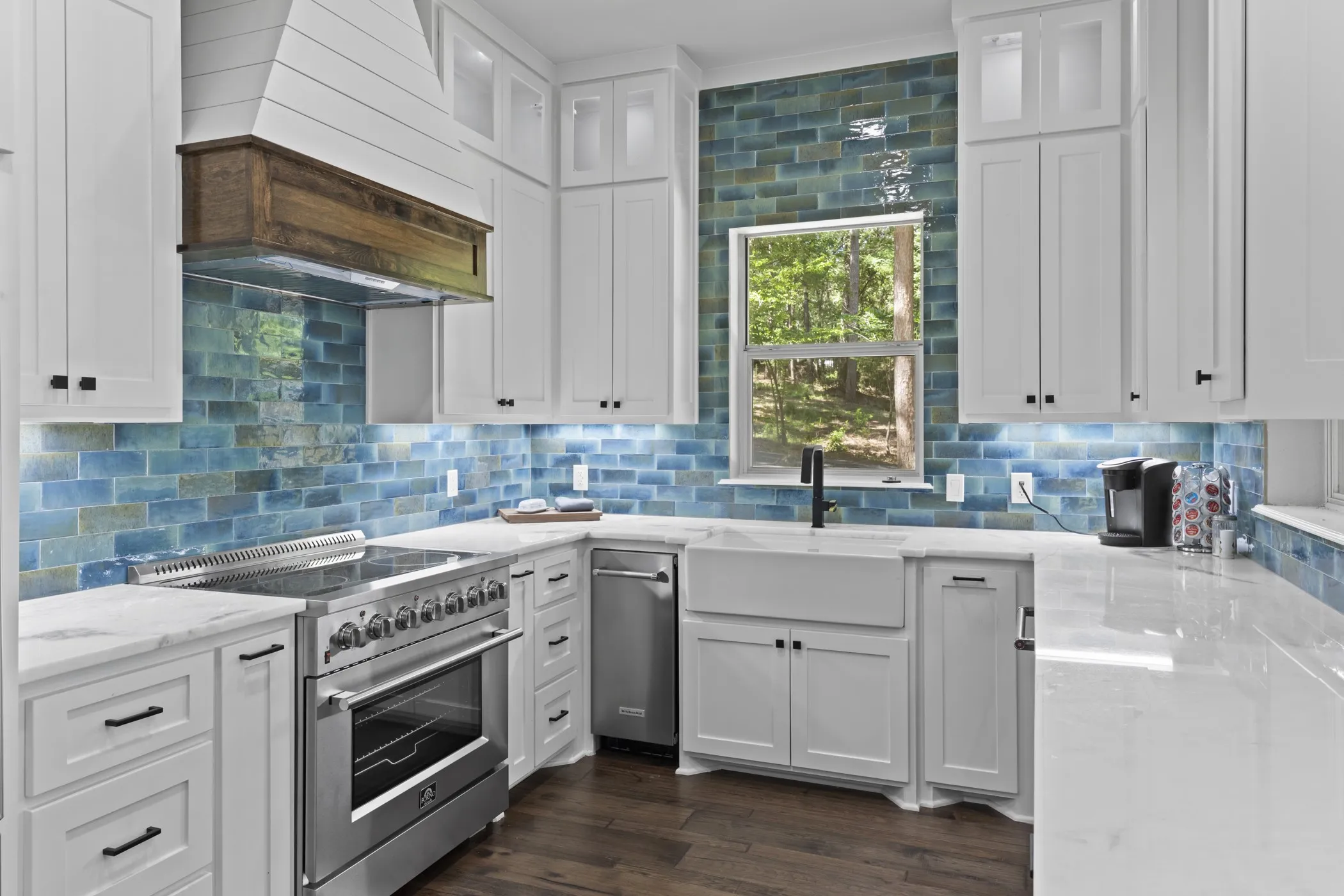 White shaker cabinetry, blue subway tile backsplash, farmhouse-style sink, stainless steel range, and wood-finish flooring