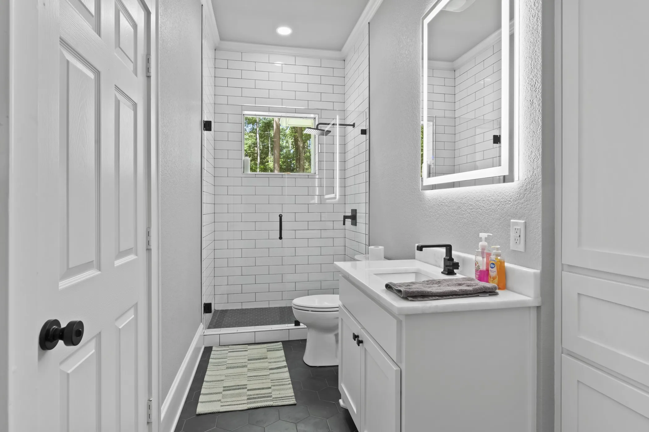 Bathroom featuring a white subway tile shower, frameless glass shower enclosure, black hexagon floor tile, and a vanity with a rectangular sink