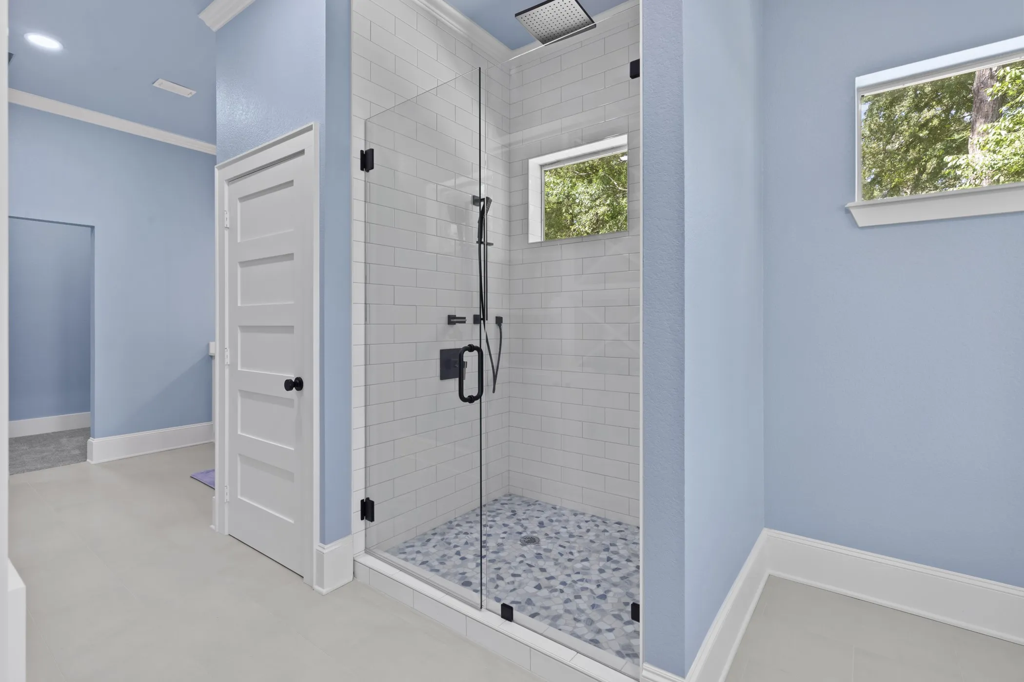 Glass-enclosed shower featuring subway tile walls, a patterned tile floor, and a matte black rainfall showerhead