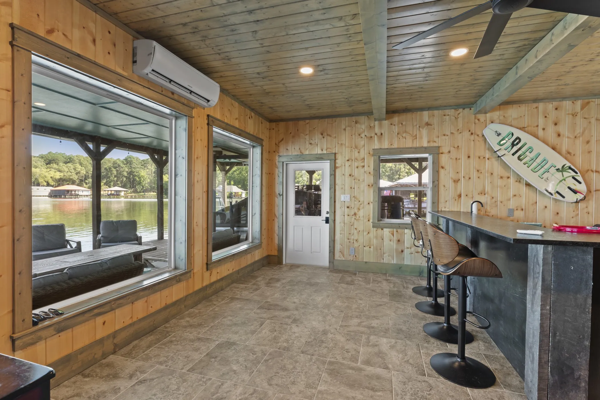 Wood-paneled interior with exposed beam ceiling, large windows, and a built-in bar