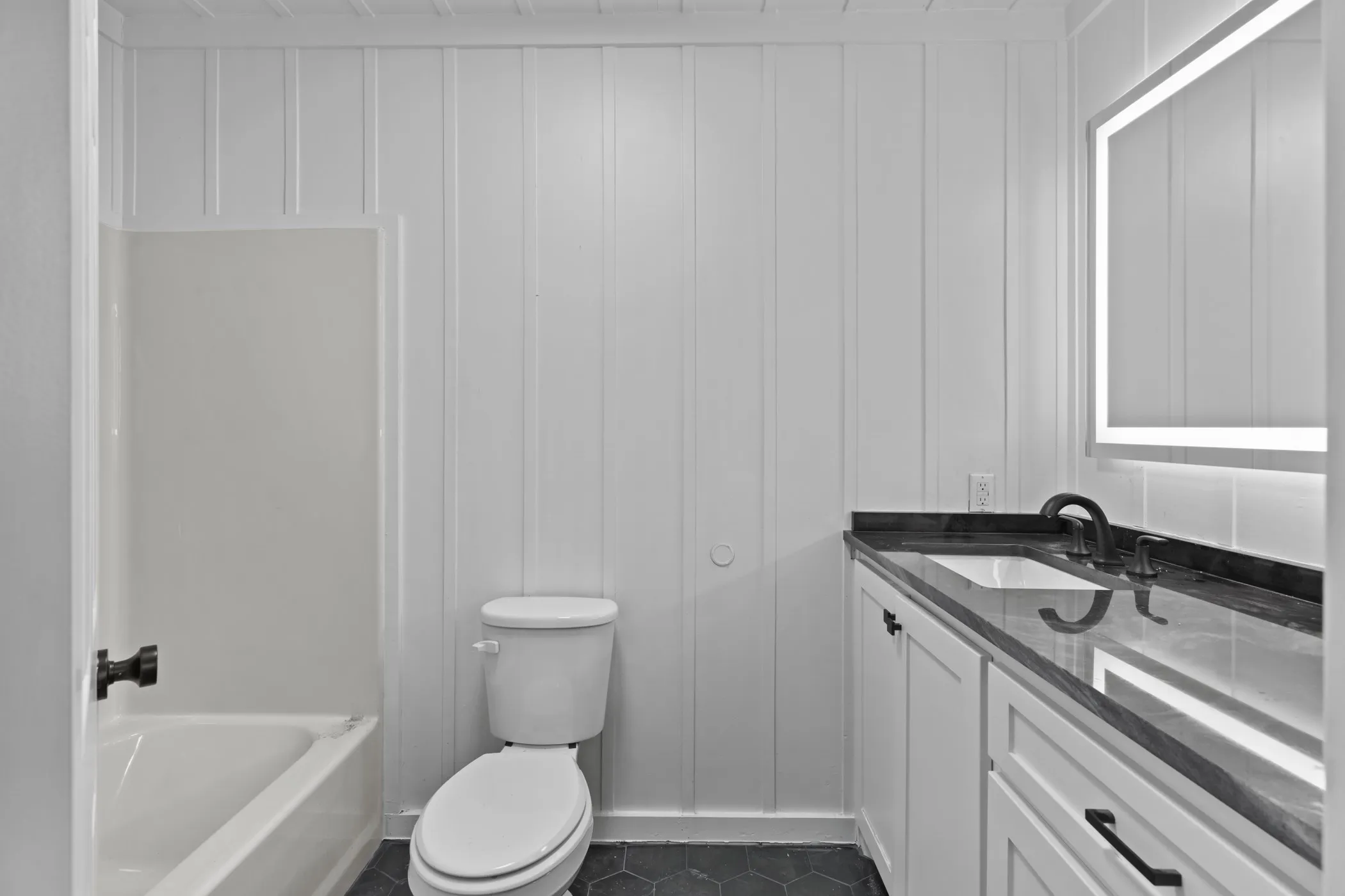 White board and batten walls, dark hexagonal floor tiling, and a white vanity with a dark countertop