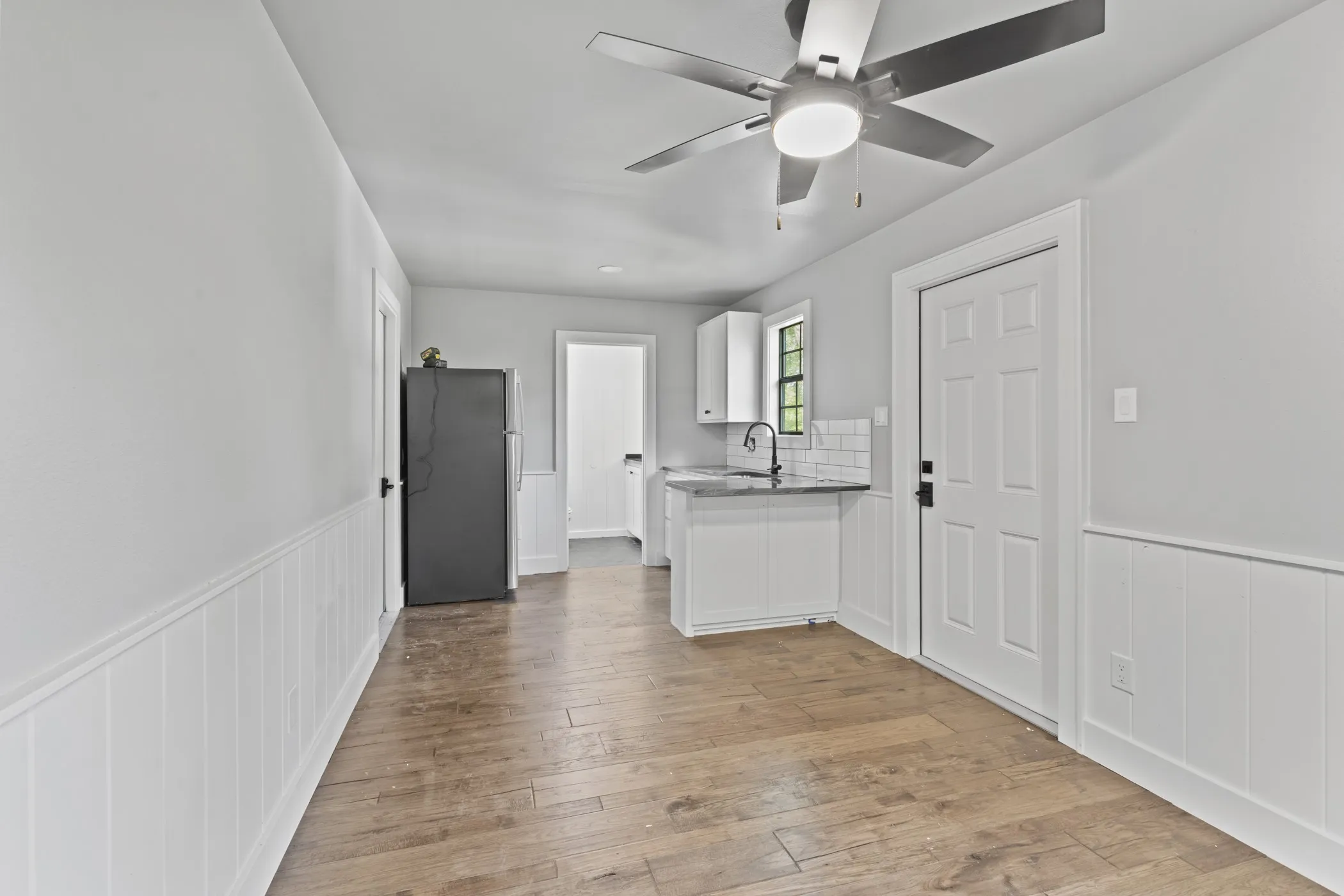 Wood-finish flooring throughout, white wainscoting, and a ceiling fan with integrated lighting