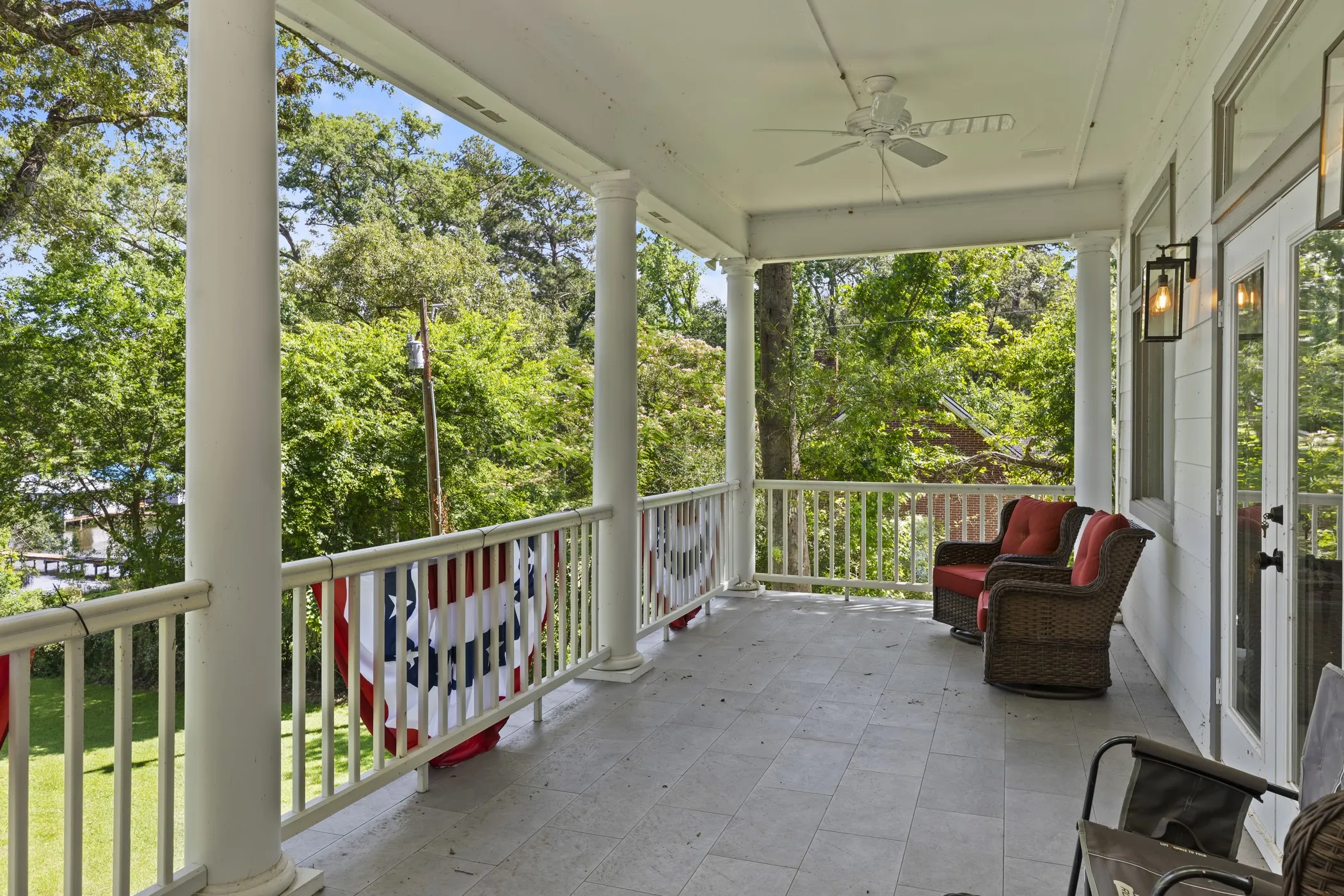 Covered porch with tile flooring, white columns, decorative railing, and ceiling fan