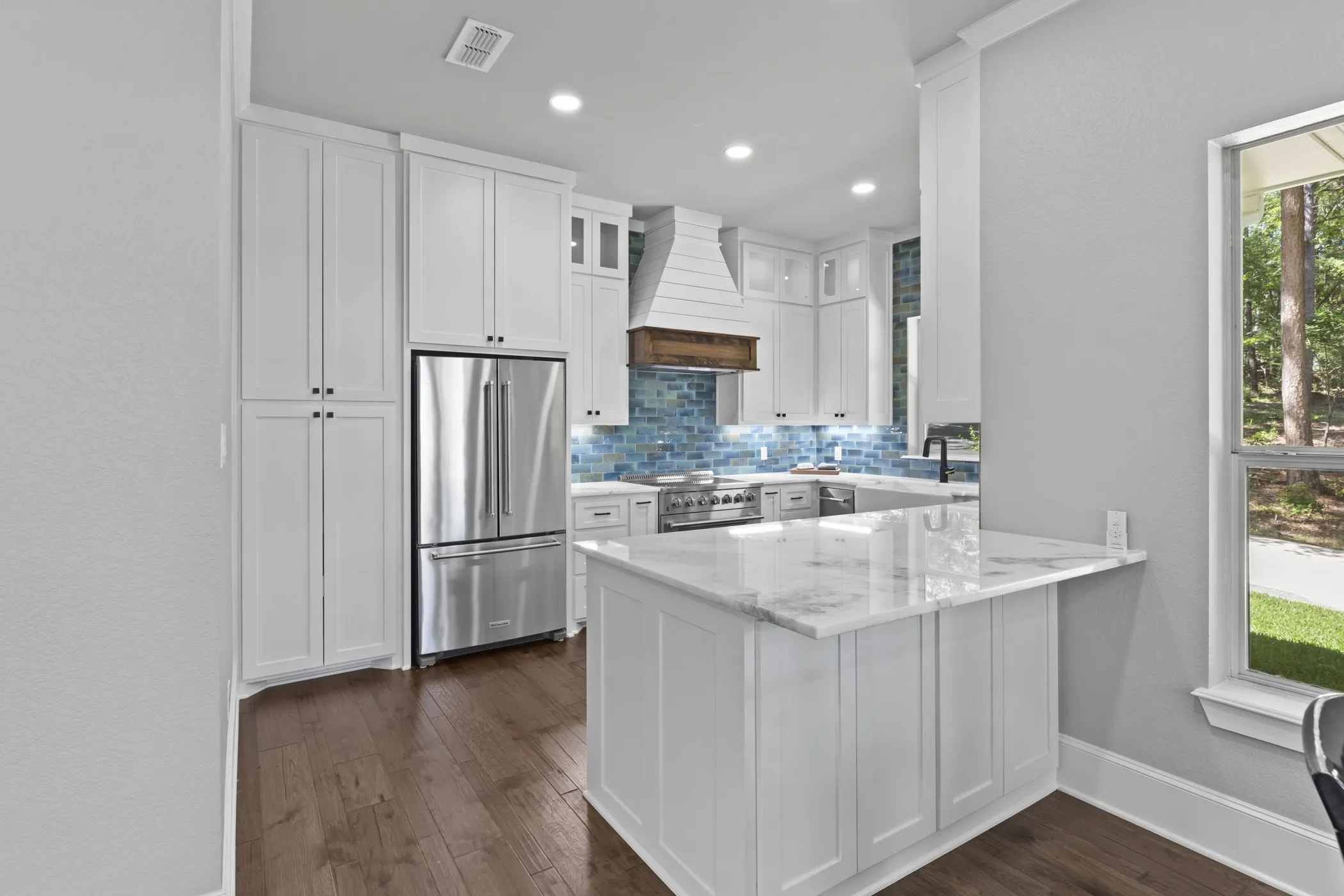 Kitchen featuring white cabinetry, stainless steel appliances, a marble-finish island, wood-finish flooring, and a blue tile backsplash