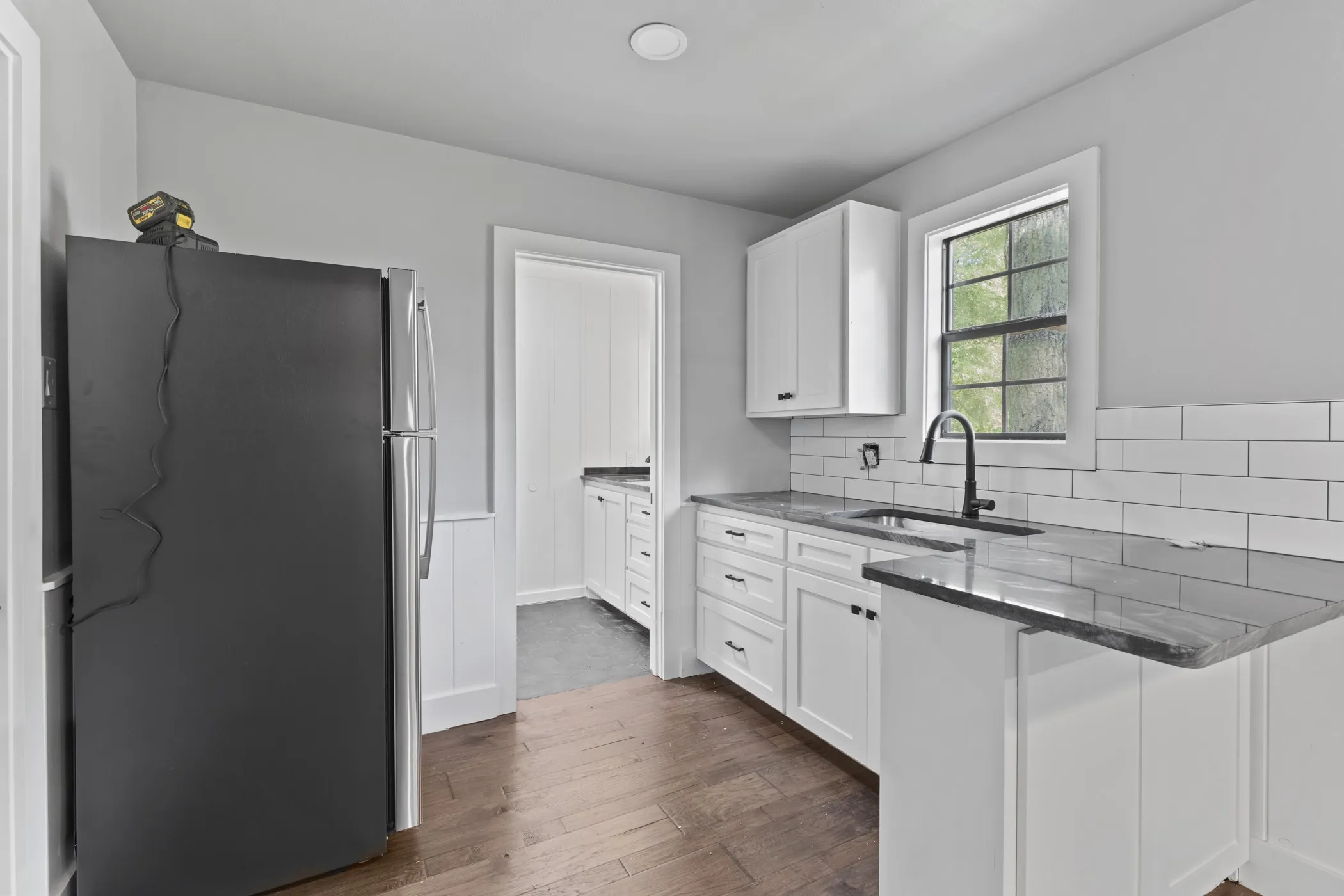 Kitchen featuring wood-finish flooring, white cabinetry with dark hardware, dark countertops, and a white subway tile backsplash