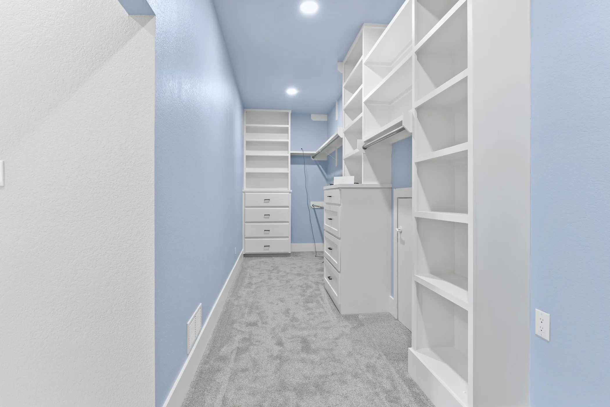 Built-in shelving, integrated drawers, recessed lighting, and carpet flooring within a spacious closet