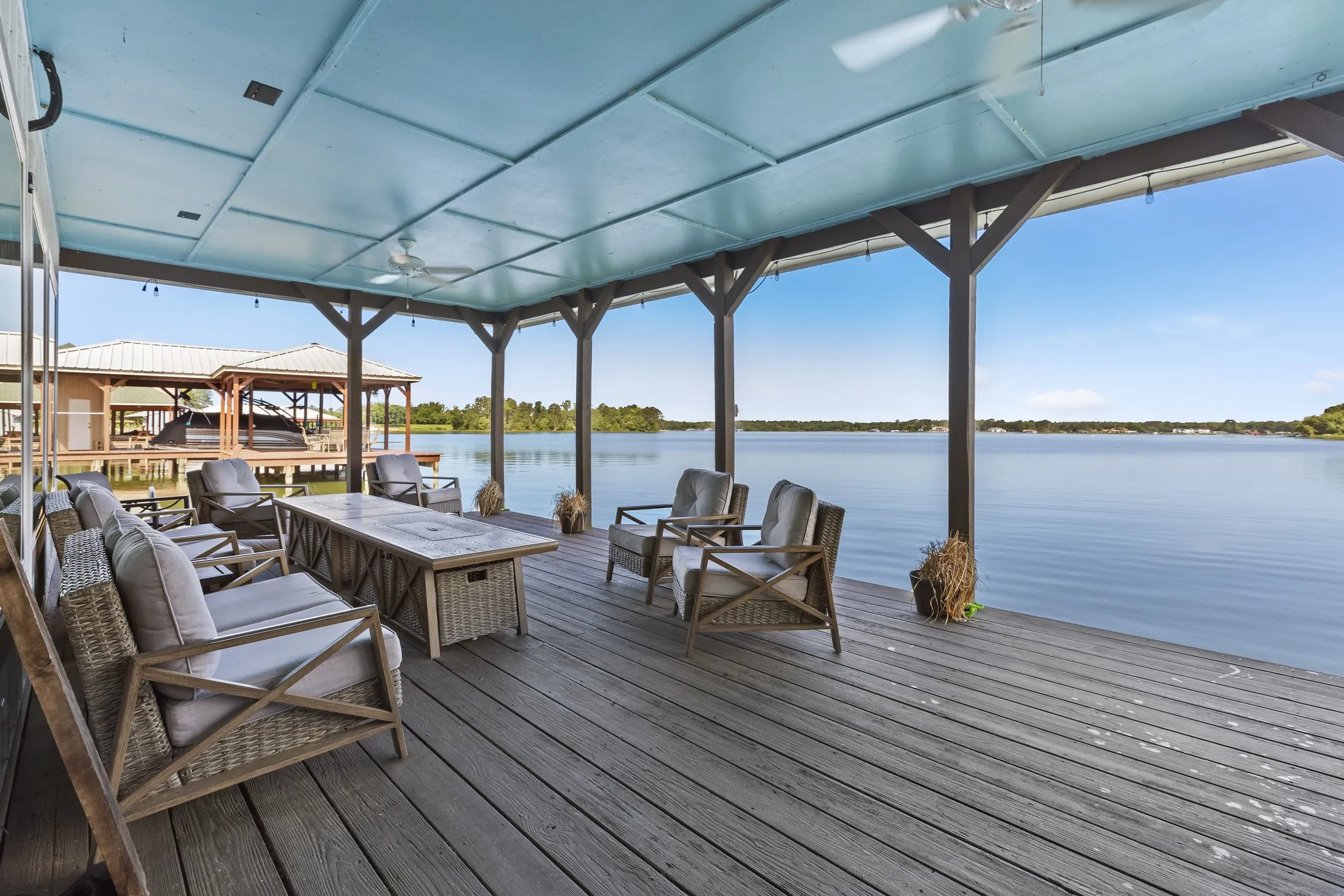 Covered outdoor deck with exposed support beams, ceiling fans, and a broad water backdrop