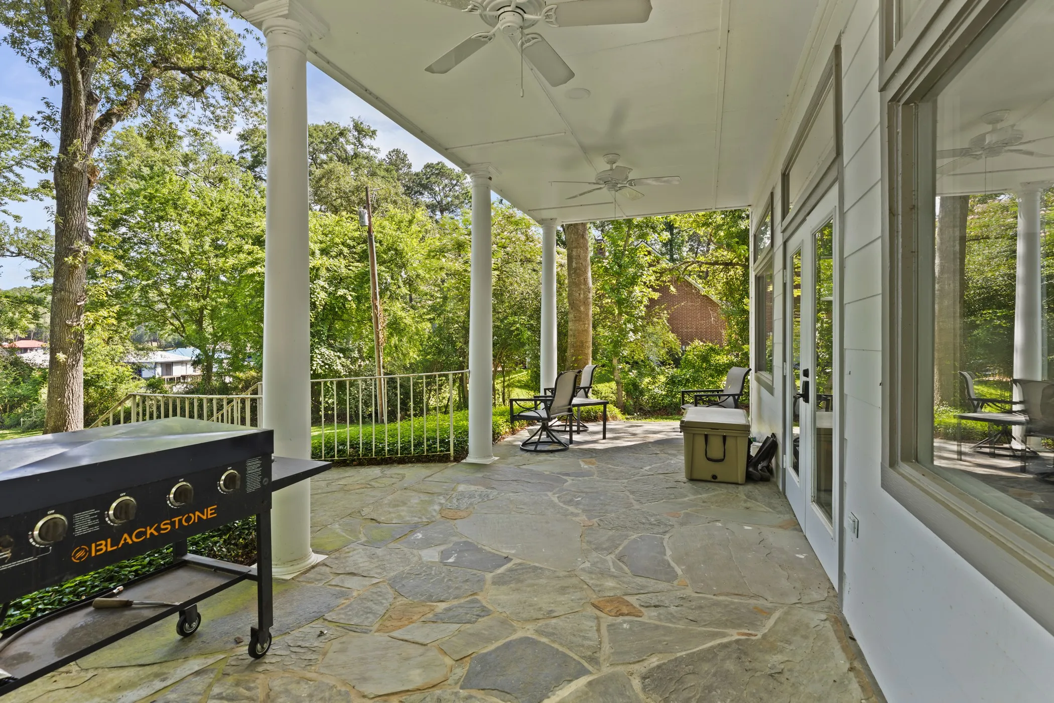 Covered patio with a flagstone surface, supported by white columns, featuring recessed lighting and ceiling fans