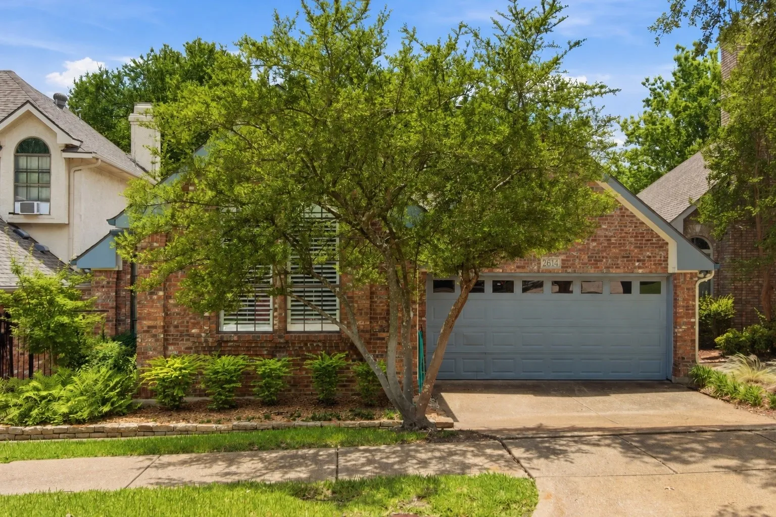 Brick exterior with a gabled roofline, integrated two-car garage, concrete driveway, and established front landscaping