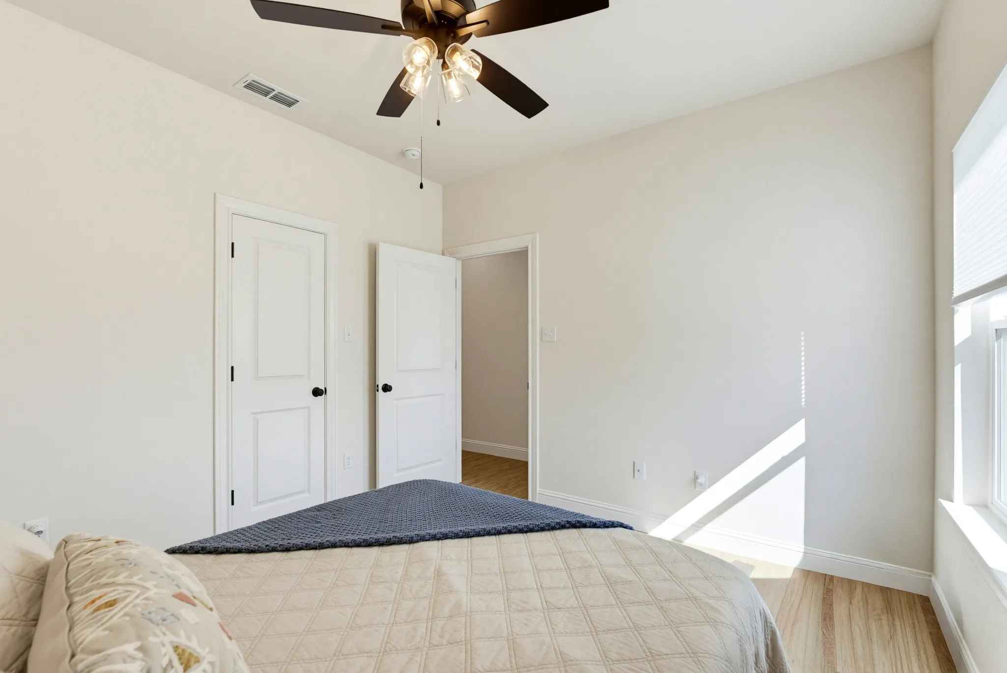 Hardwood-finish flooring, ceiling fan with light fixture, window with blinds, and white interior doors with black hardware