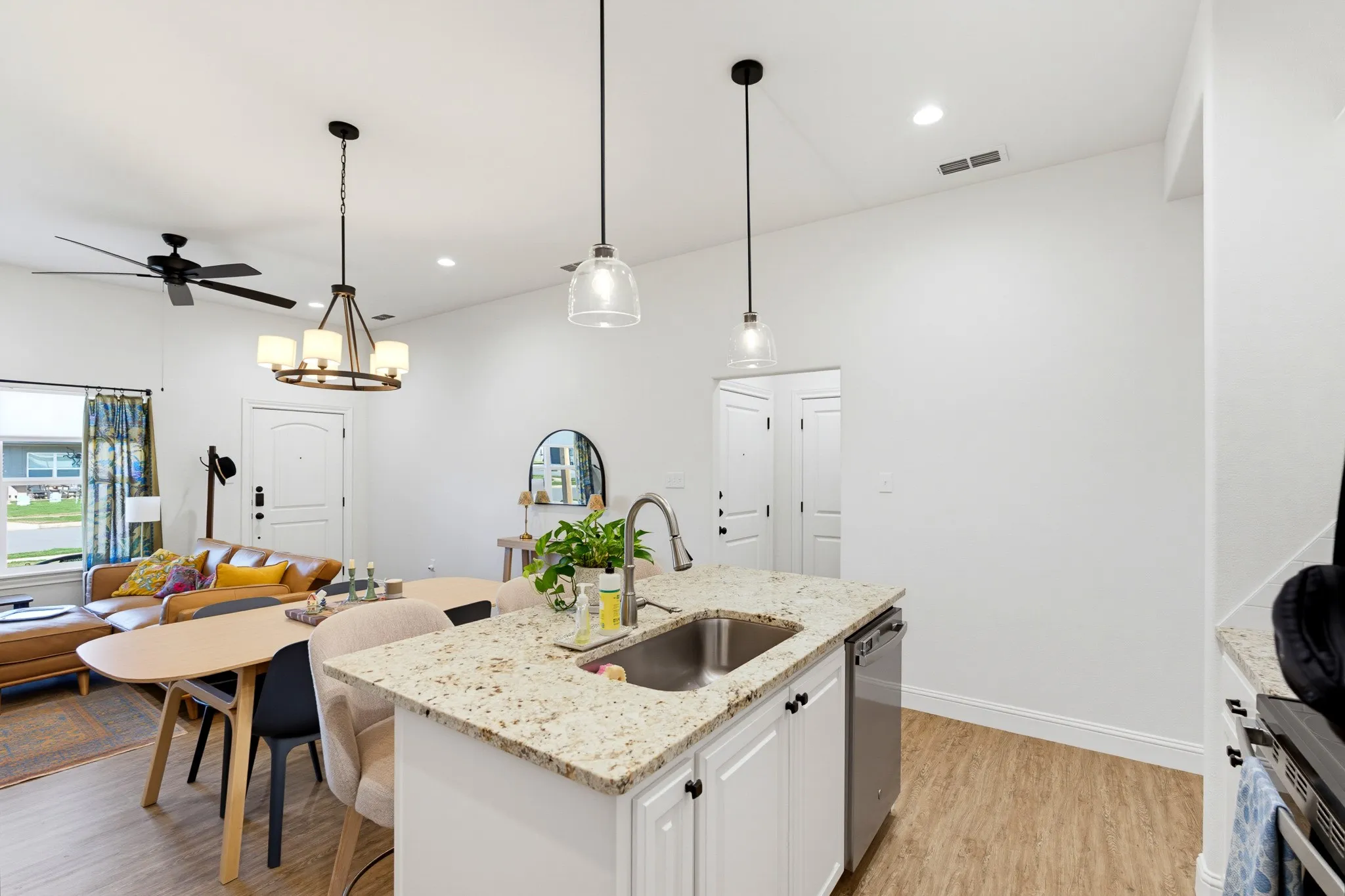Kitchen island with granite countertop and stainless steel sink, white cabinetry with dark hardware, recessed lighting, and wood-finish flooring