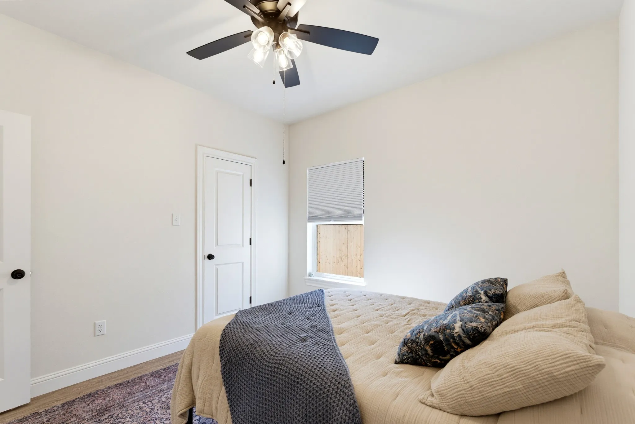 Ceiling fan with integrated lighting, wood-finish flooring, and a single window with roller shade